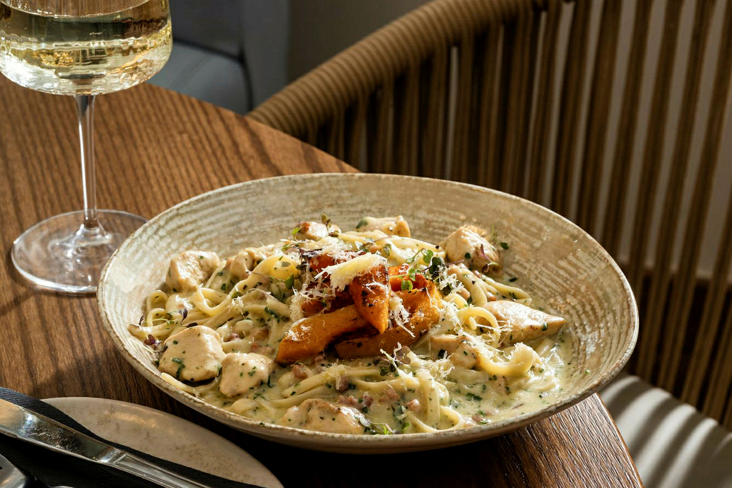 En tallerken med pasta med kremet saus og tilbehør, servert på et spisebord med et glass hvitvin. (AI-generert tekst)