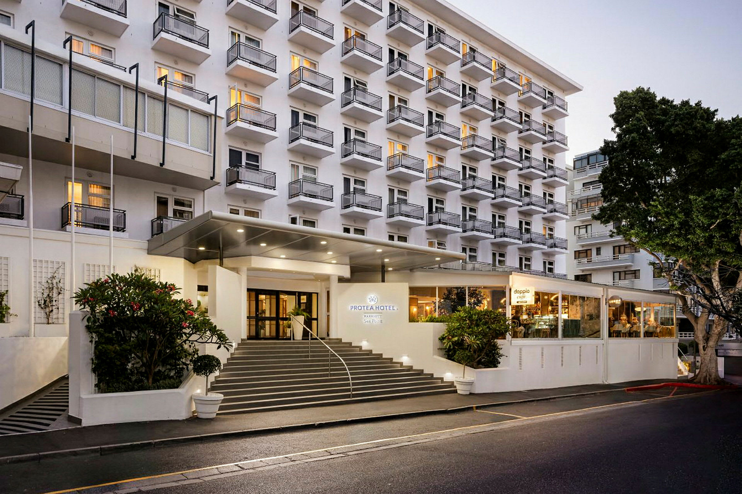 Hotellbygning med flere etasjer og balkonger, samt en opplyst inngang og trapp foran. (AI-generert tekst)