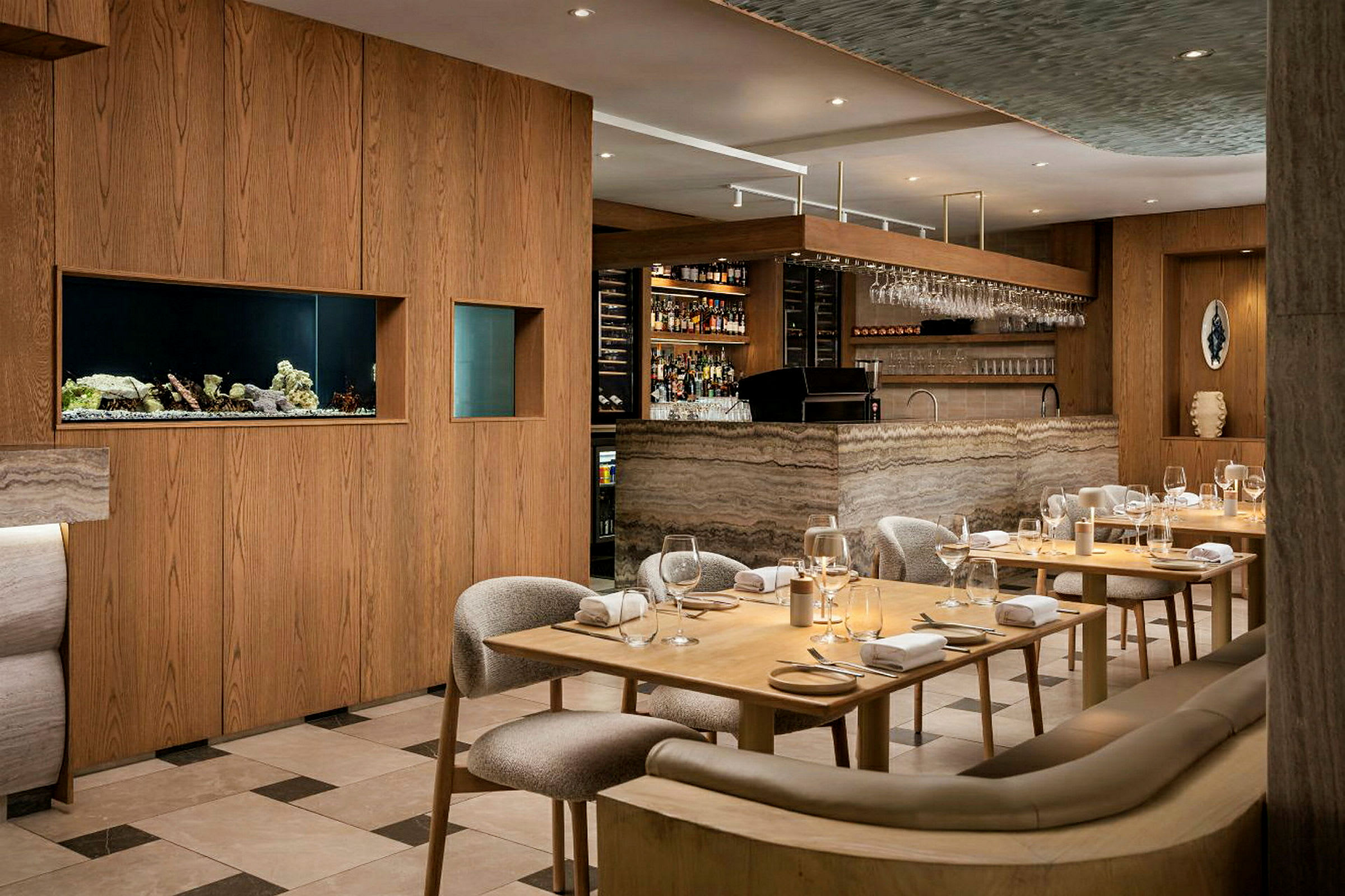 Et elegant restaurantinteriør med tremøbler og en bardisk i marmordesign. Bordene er dekket med glass og servietter. (AI-generert tekst)