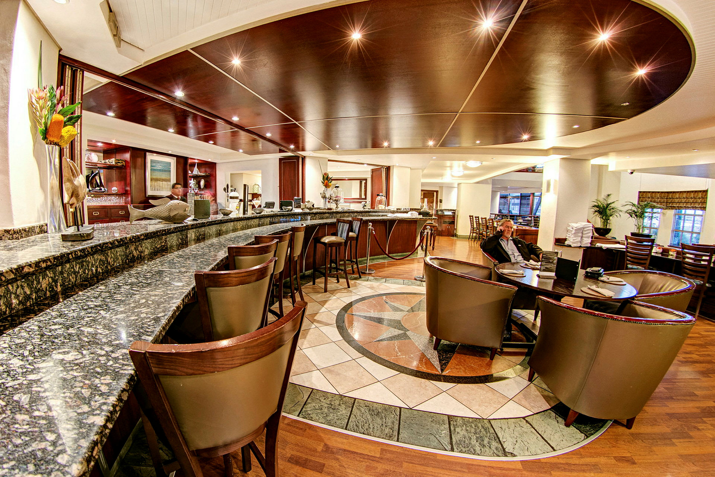 Et elegant hotellbarområde med marmordisk, mørke tremøbler og loungeområde. (AI-generert tekst)