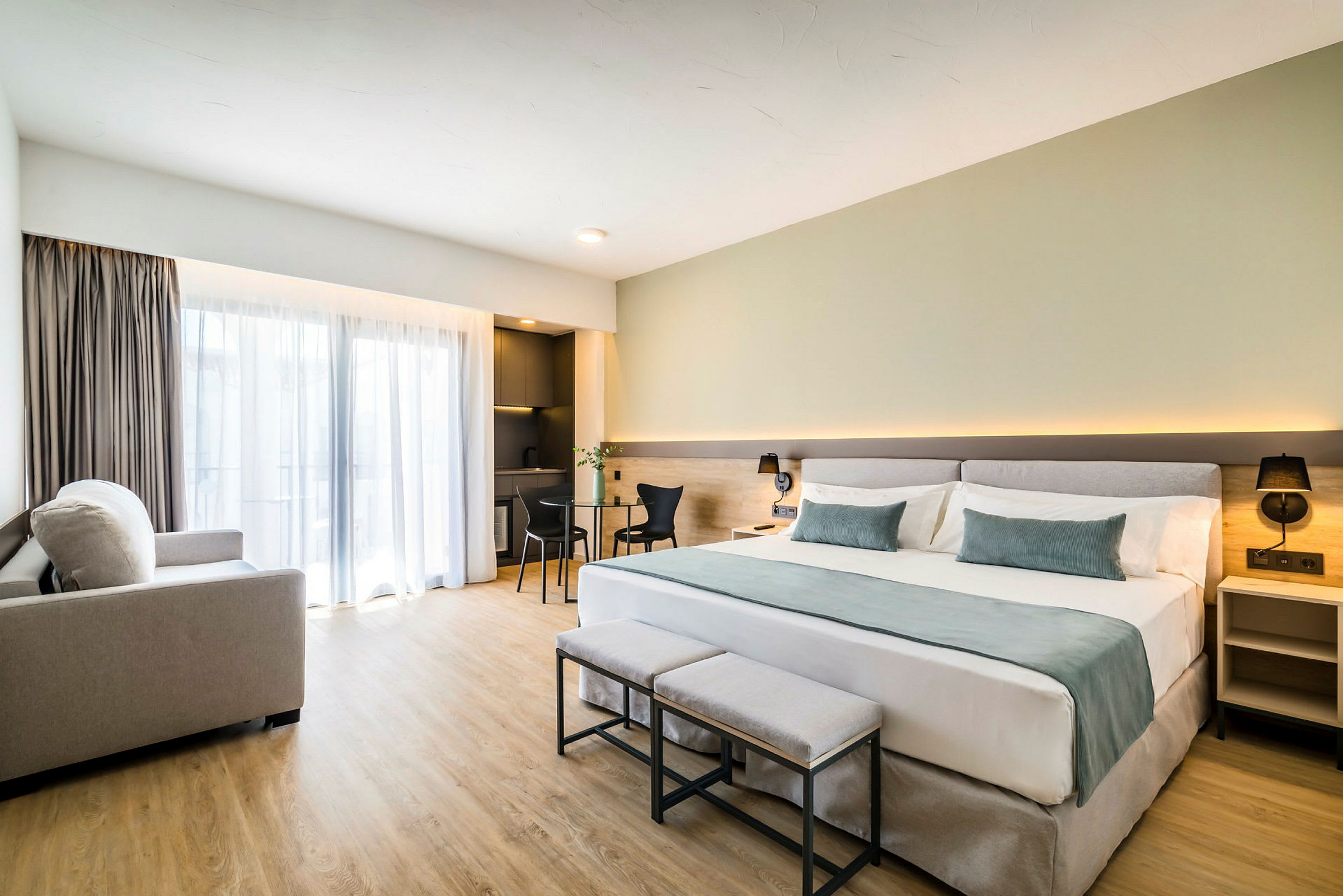 Et moderne og lyst hotellrom utstyrt med en stor seng, et skrivebord og en sittegruppe med utsikt fra et stort vindu. (AI-generert tekst)