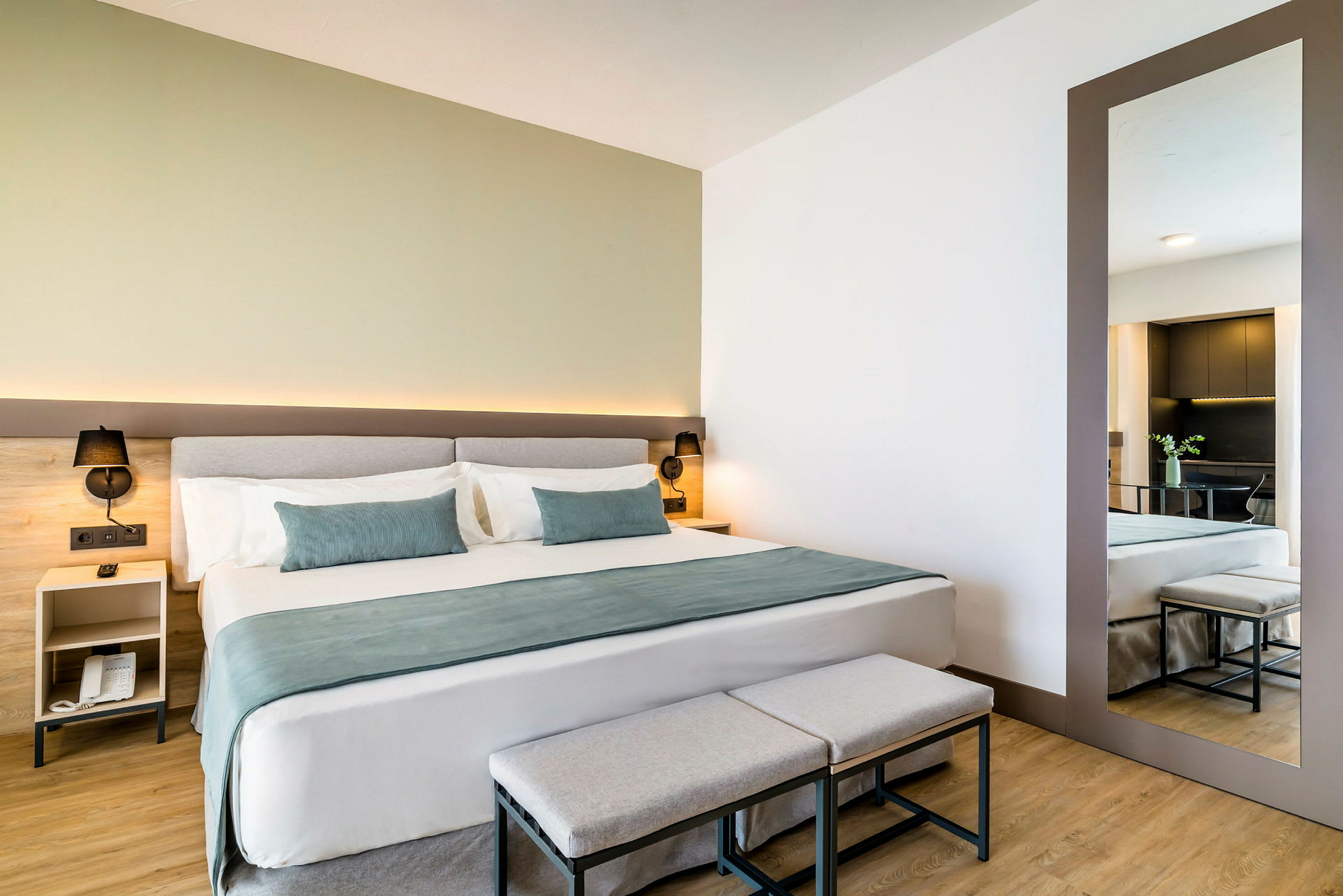 Et moderne hotellrom med en dobbeltseng, to krakker foran sengen og et stort speil på veggen. (AI-generert tekst)