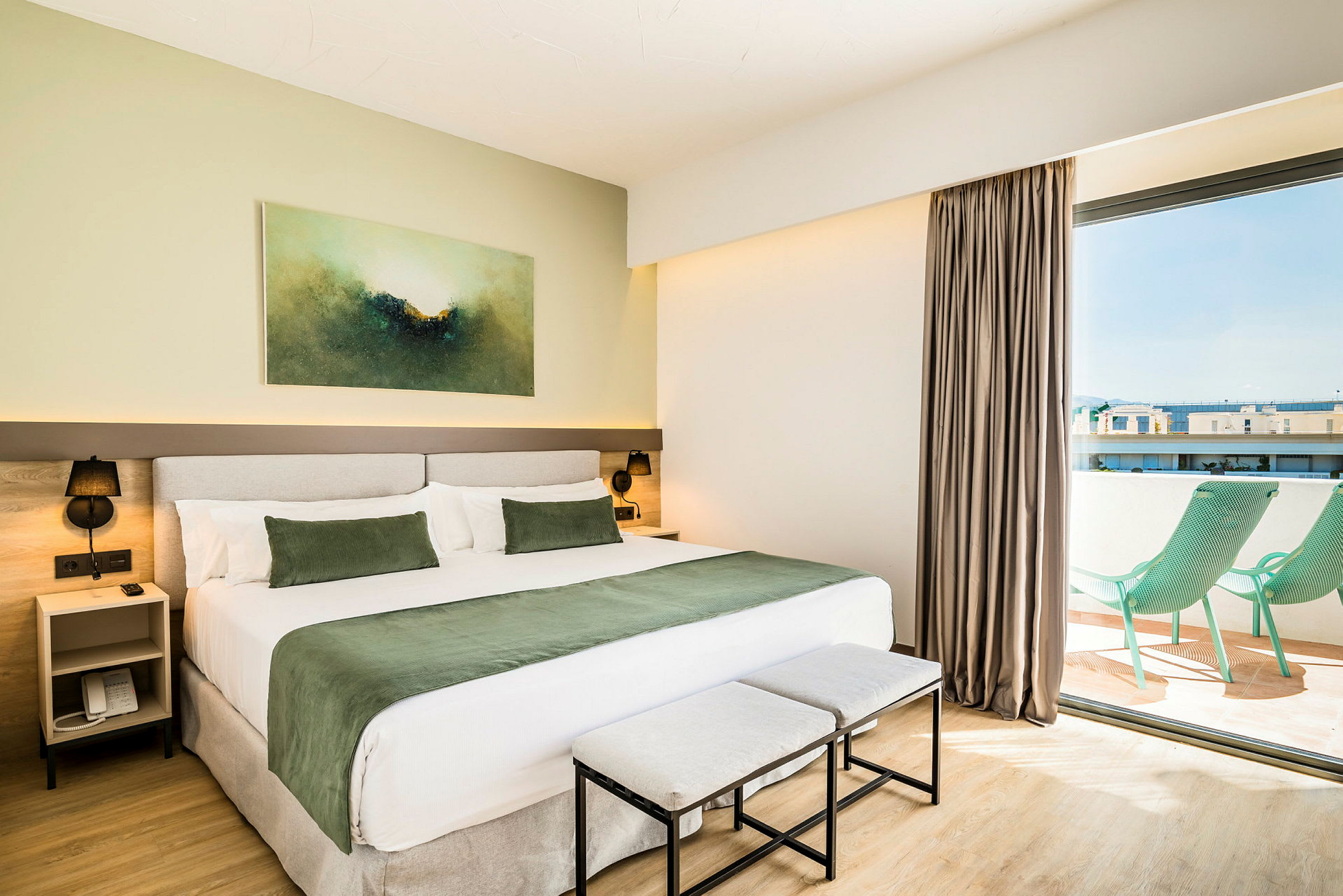 Bilde av et moderne hotellrom med en stor seng, grønt sengeteppe og puter, samt et kunstverk på veggen. Rommet har en balkong med to grønne solsenger. (AI-generert tekst)