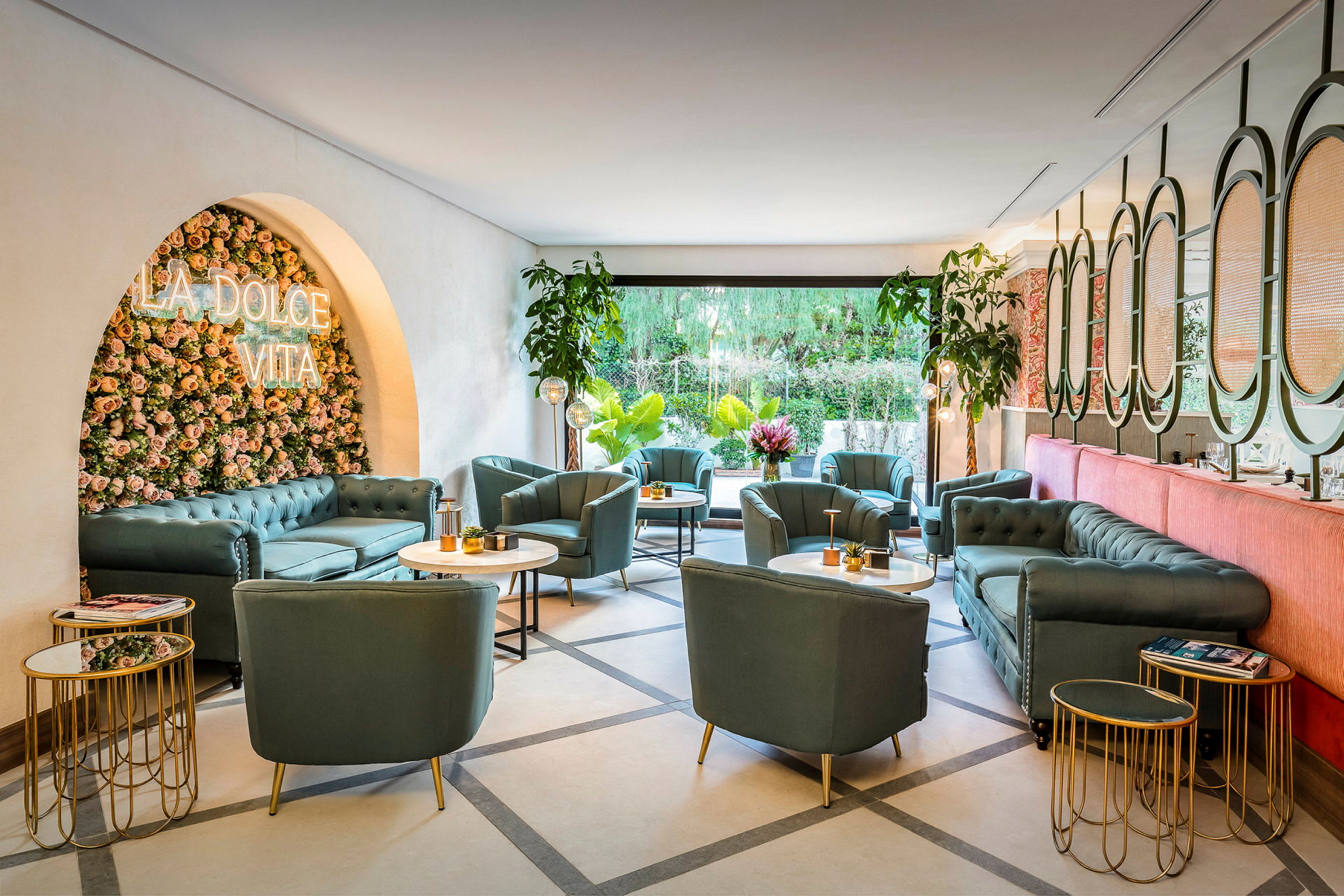 En loungeområde med grønne sofaer og stoler, marmorbord og plantepynt. En dekorasjonsvegg med teksten "La Dolce Vita" pryder rommet. (AI-generert tekst)