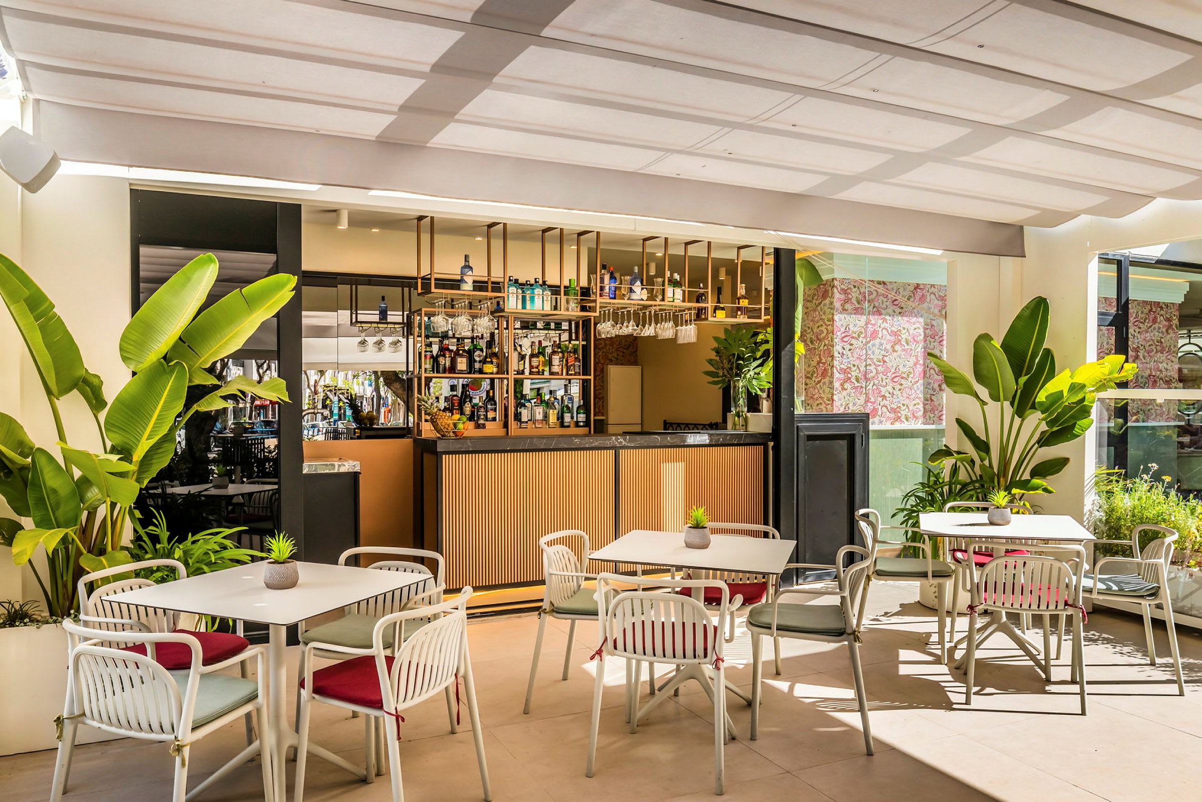 En bar med sitteplasser og bord, omgitt av store grønne planter og med dekorative elementer. (AI-generert tekst)