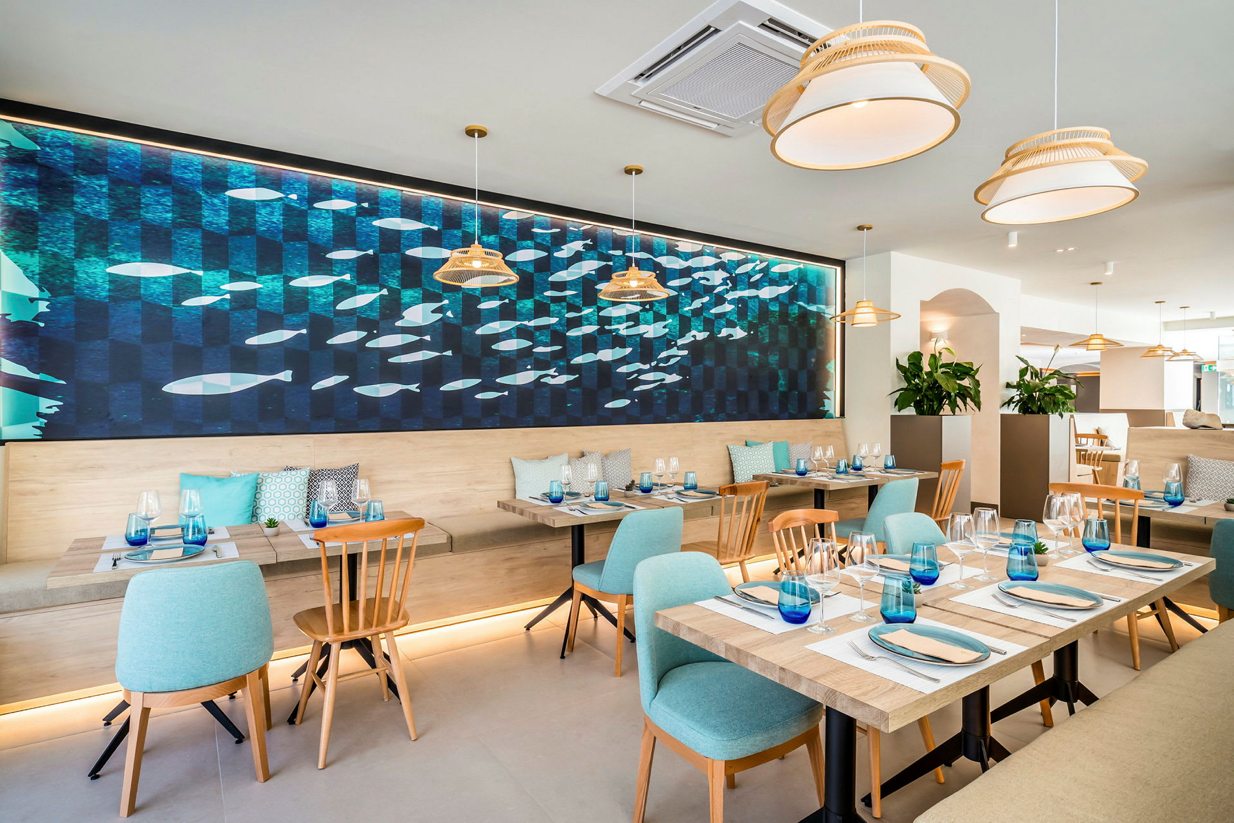 Et moderne innredet restaurantområde med bord og stoler, samt en stor veggdekorasjon med fiskemotiv. (AI-generert tekst)