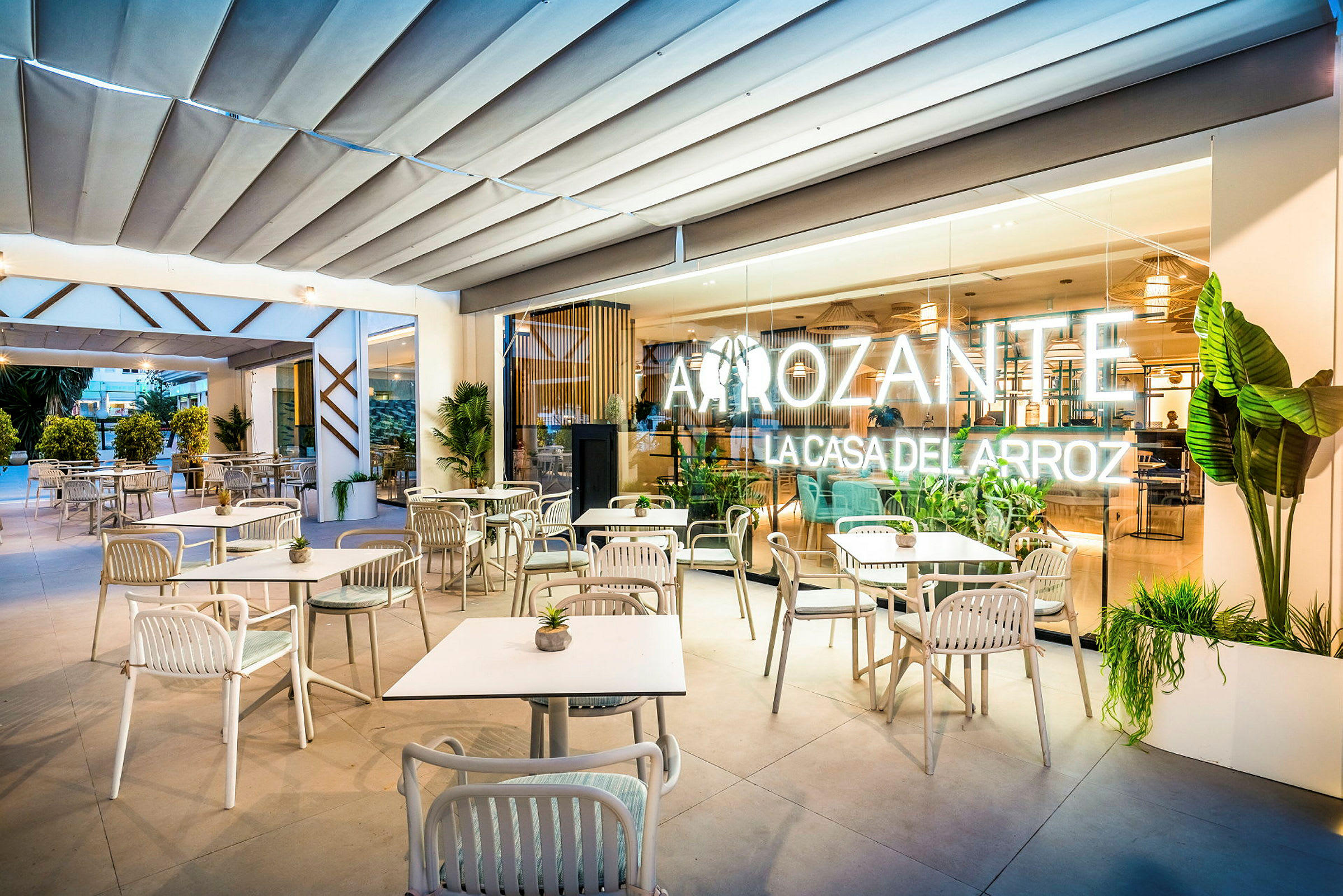 En restaurant med uteservering som har hvite bord og stoler på en overbygd terrasse. (AI-generert tekst)
