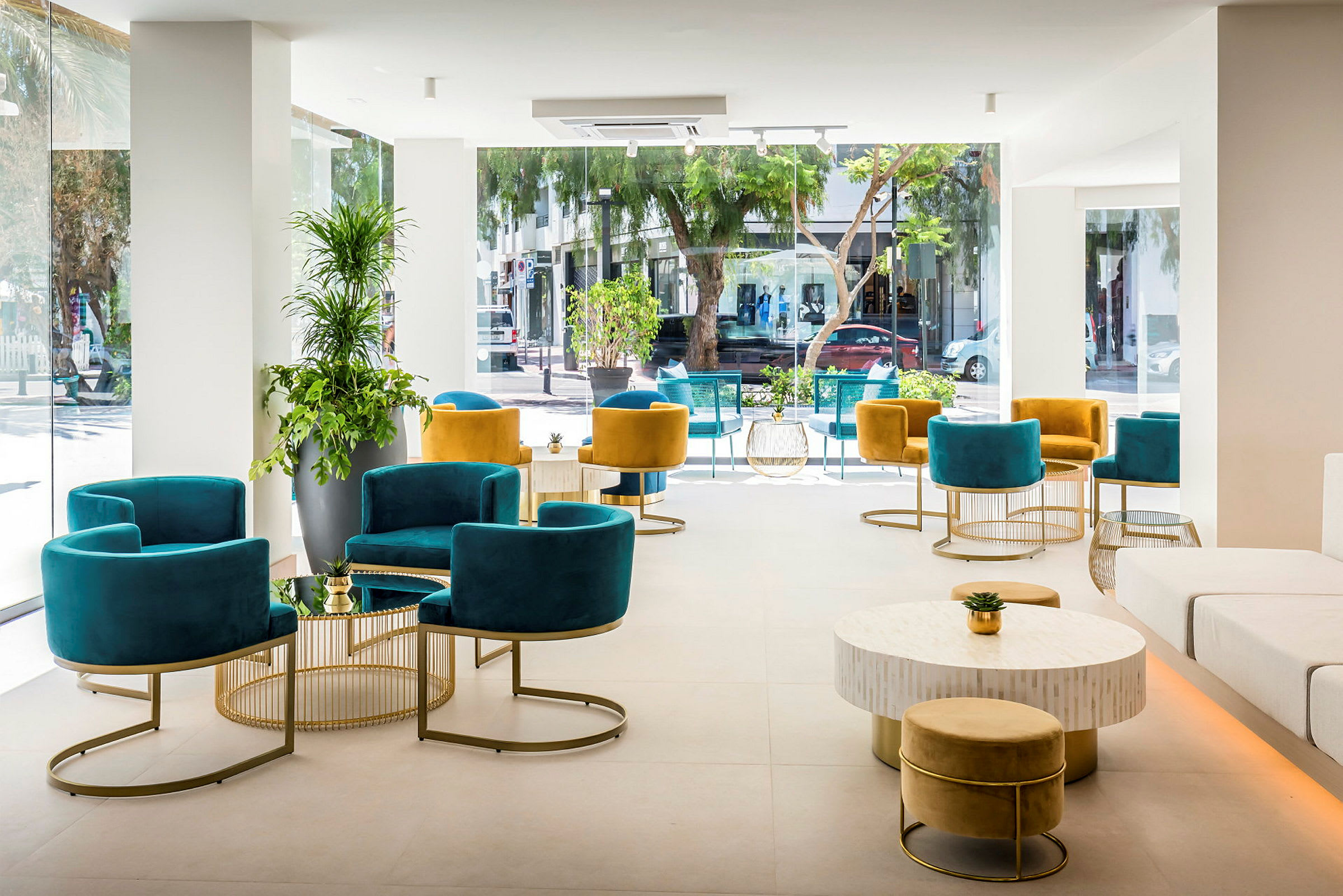 Interiør av en lys og moderne lounge med fargerike stoler og bord, store vinduer som vender ut mot et bymiljø. (AI-generert tekst)