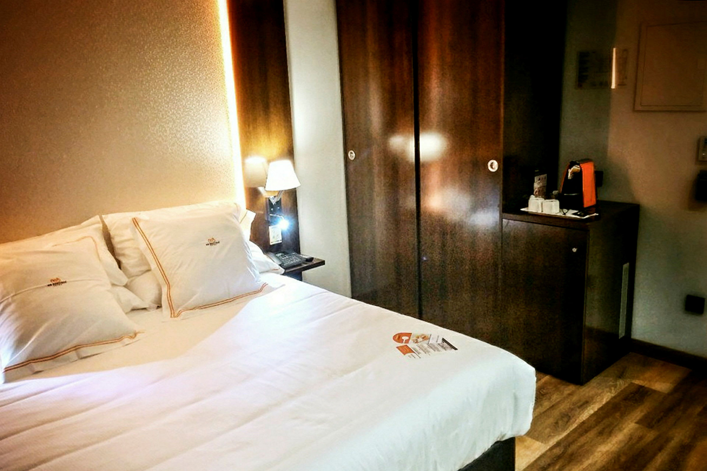 Et hotellrom med en seng og opplyst nattlampe ved siden av et mørkt treskap. (AI-generert tekst)