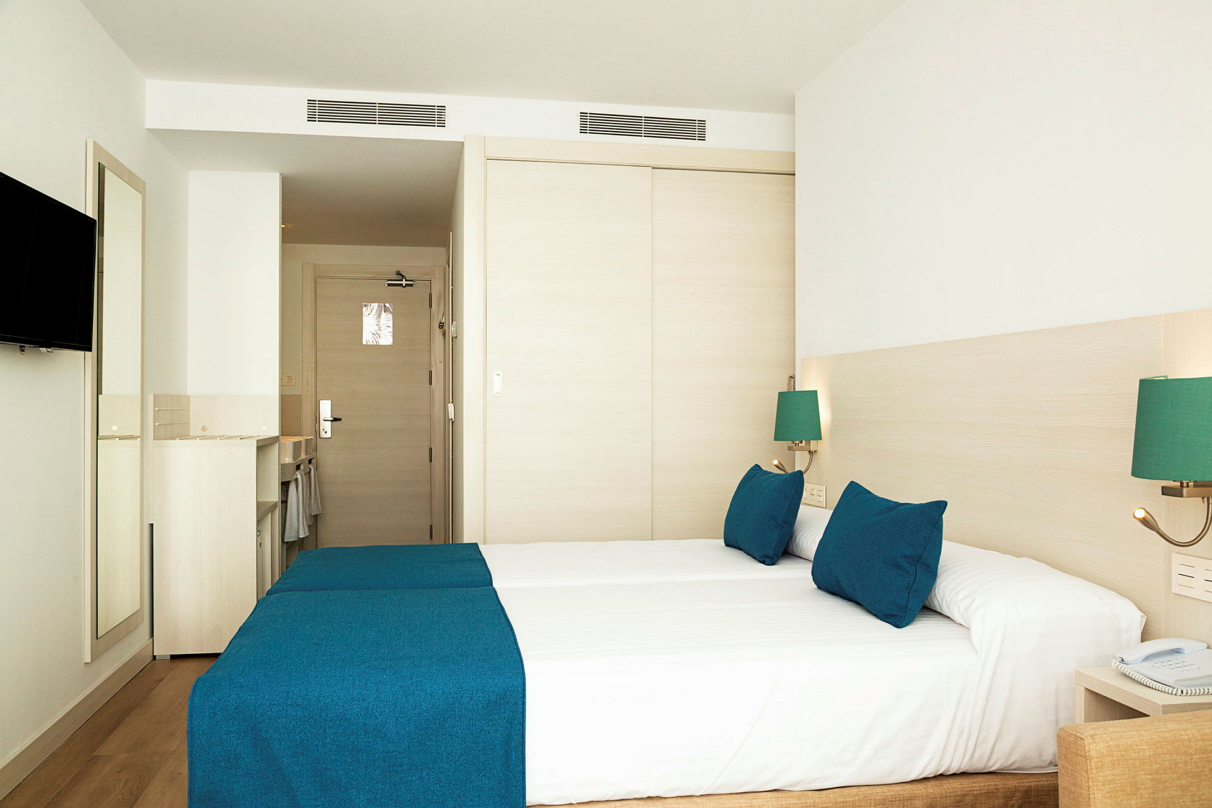 Hotellrom med to senger dekket med blå sengetepper og matchende puter. (AI-generert tekst)