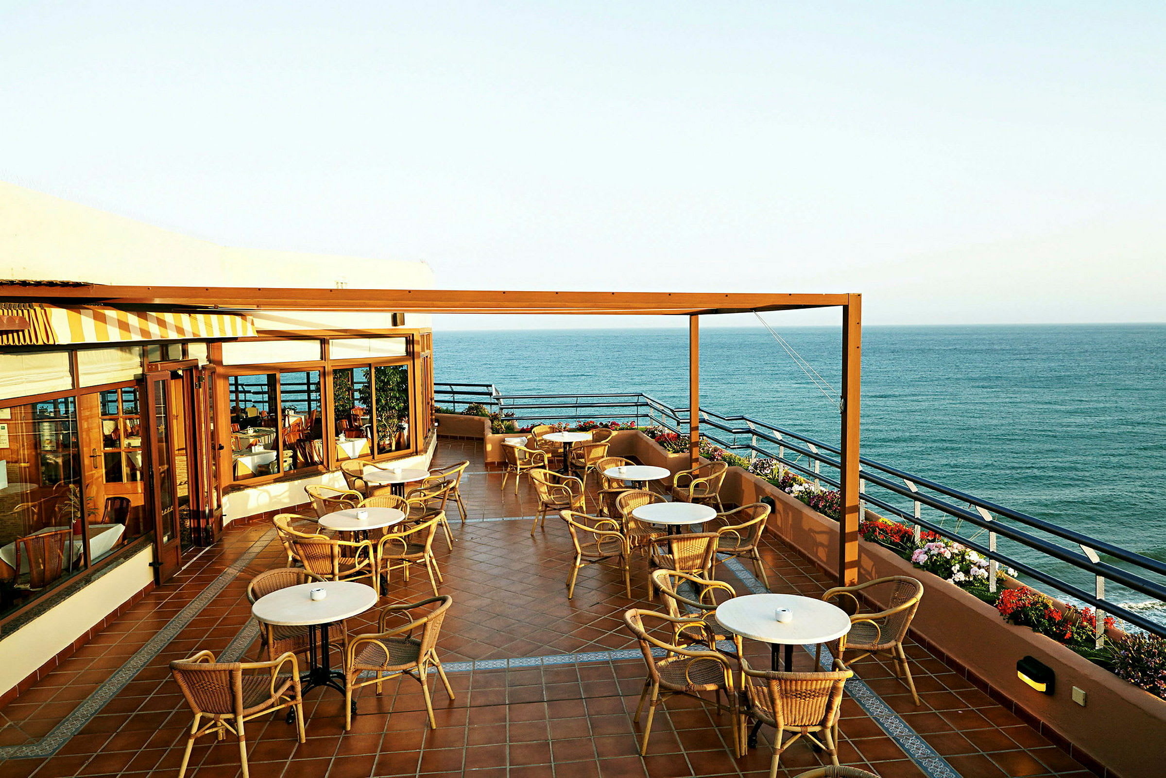 En terrasse med bord og stoler og utsikt over havet. (AI-generert tekst)