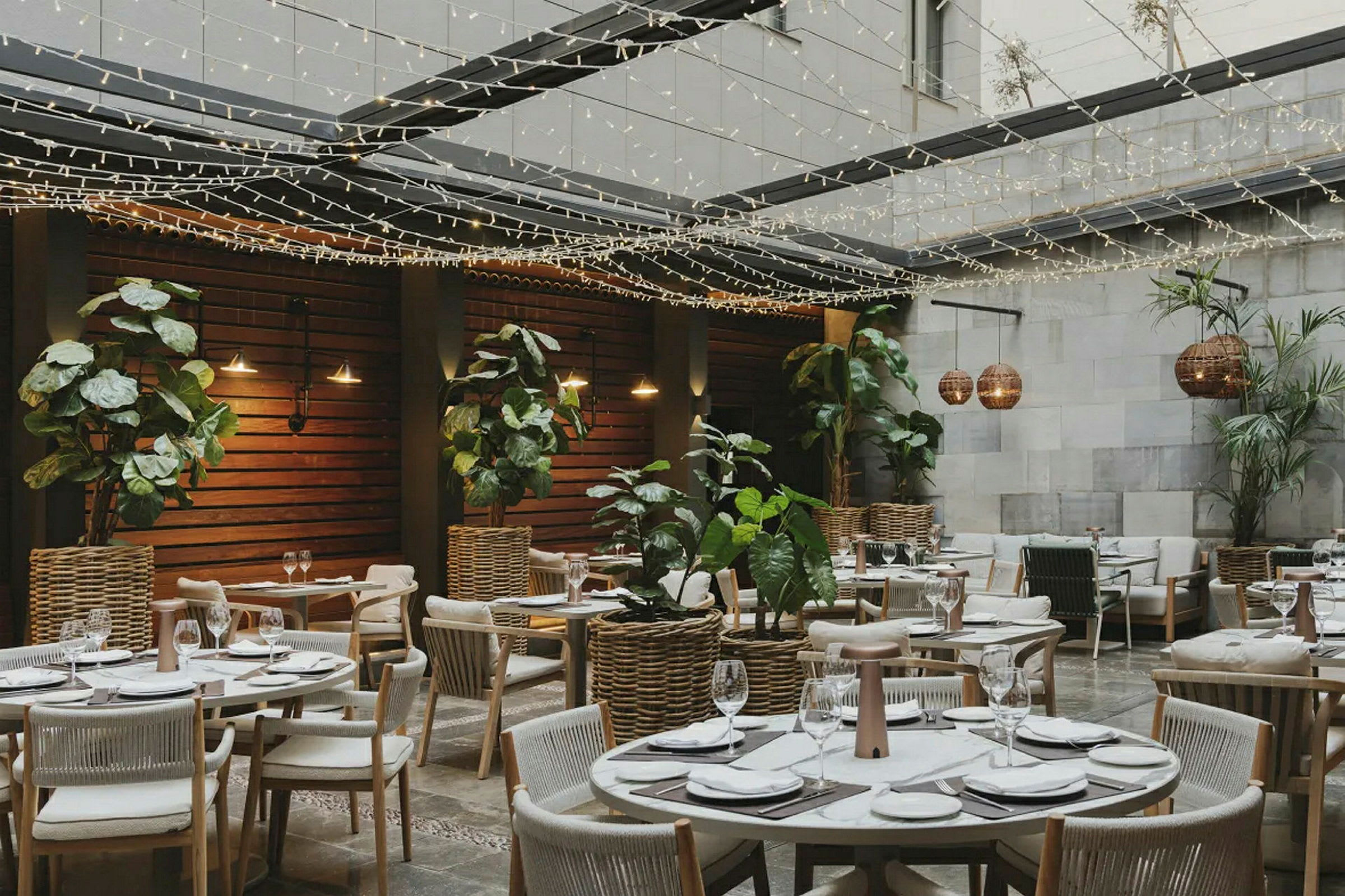 En restaurant med uteområde, bord dekorert for måltider omgitt av planter og lyslenker. (AI-generert tekst)