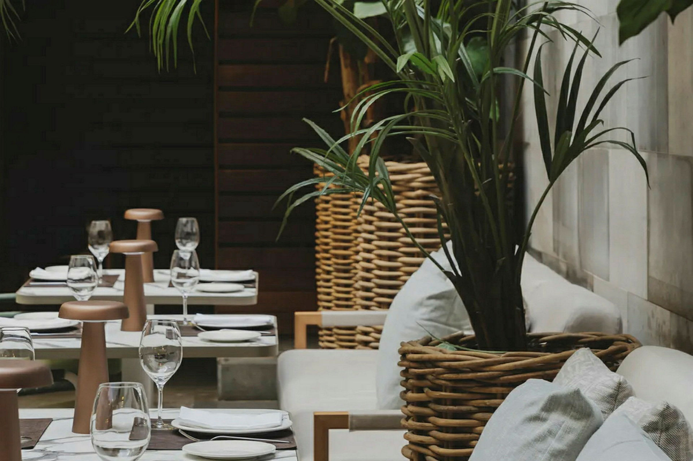 En uteplass med dekkede bord og komfortable stoler omgitt av planter i kurvkrukker. (AI-generert tekst)
