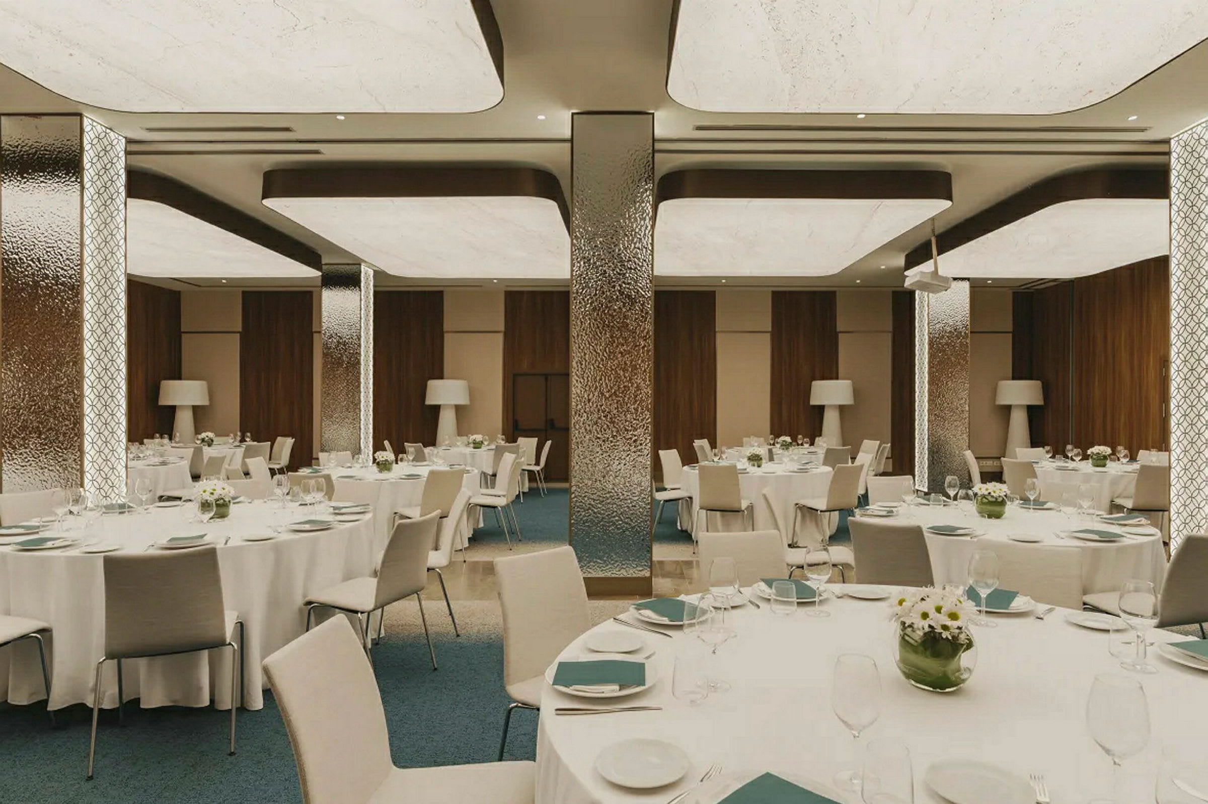 En elegant spisesal med dekkede runde bord, dekorert med blomster og serveringsartikler, omgitt av moderne interiørdetaljer. (AI-generert tekst)