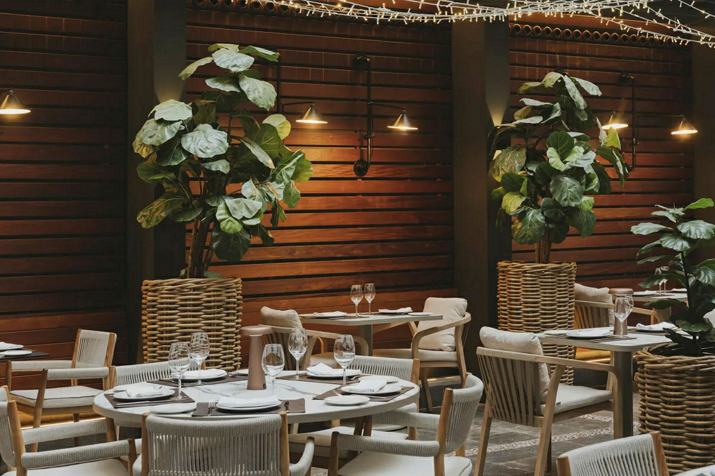 En opplyst restaurant med trepanel, plantepynt og dekkede bord. (AI-generert tekst)