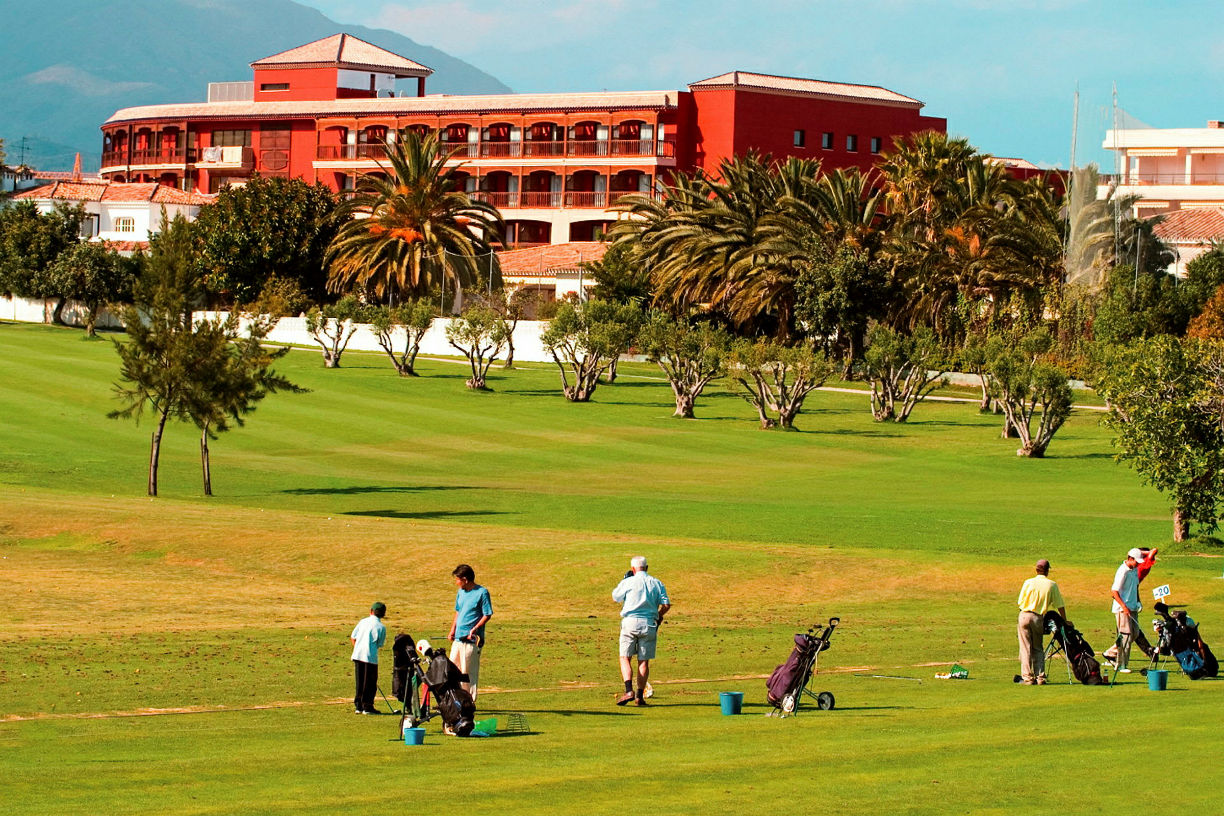Personer spiller golf på en frodig golfbane foran et rødt hotell. (AI-generert tekst)