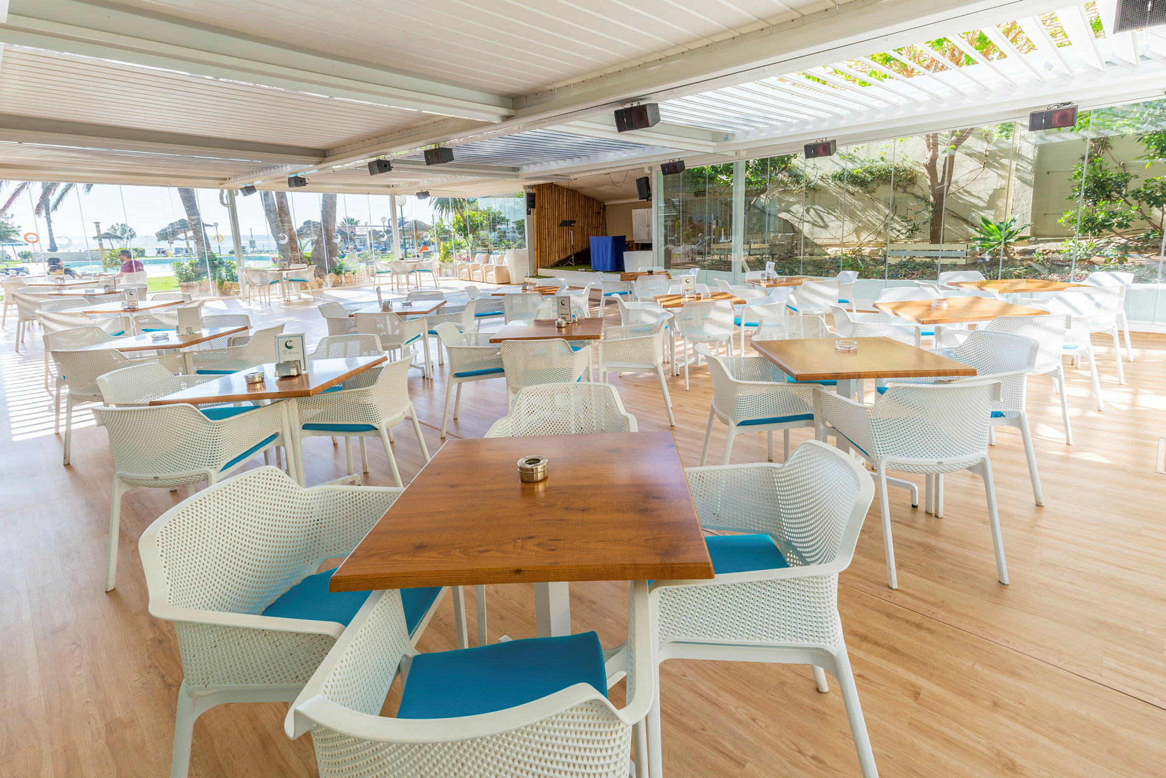 Utendørs restaurant med bord og stoler foran panoramavinduer. (AI-generert tekst)
