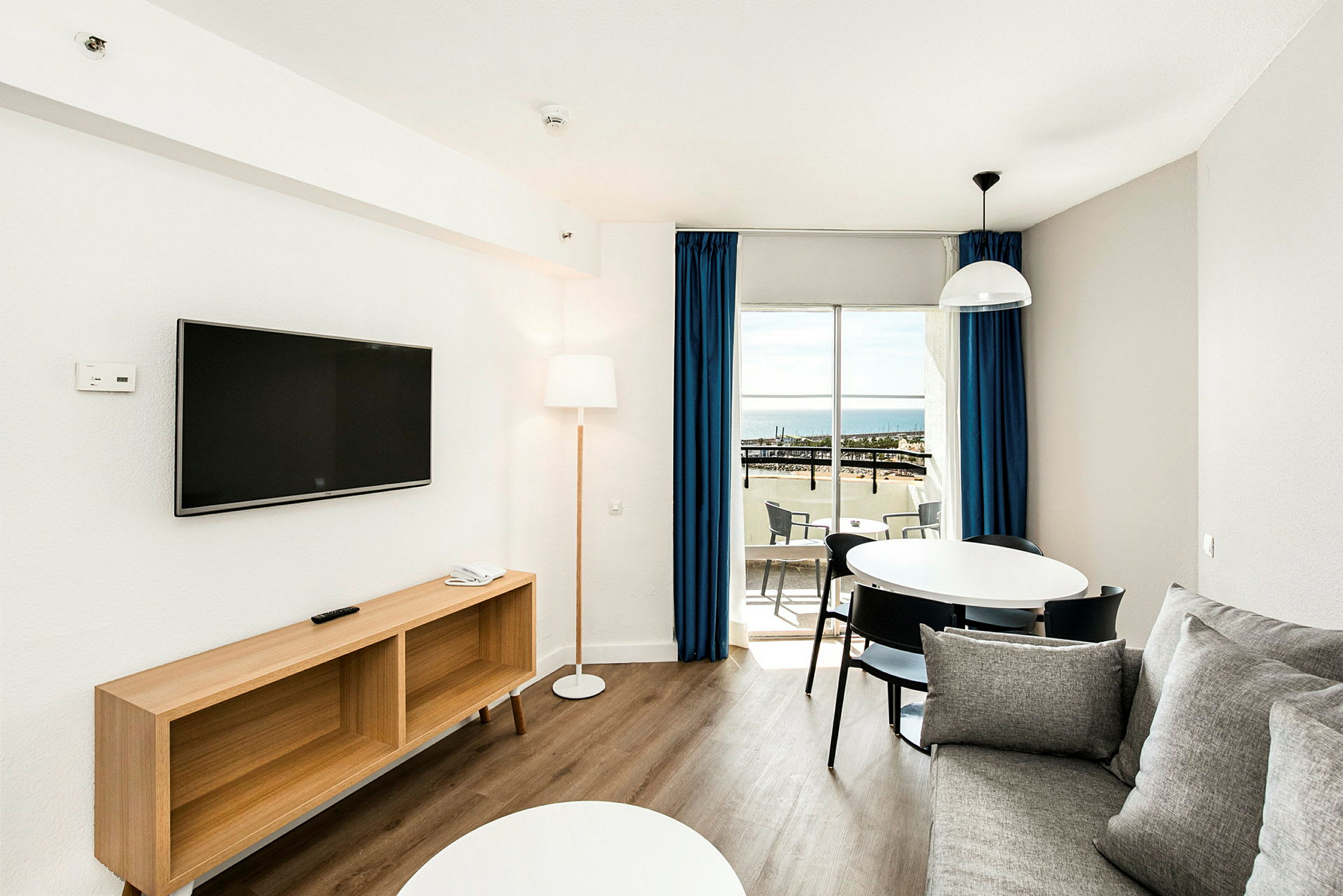En moderne stue med sofa, TV, spisebord og balkong med havutsikt. (AI-generert tekst)