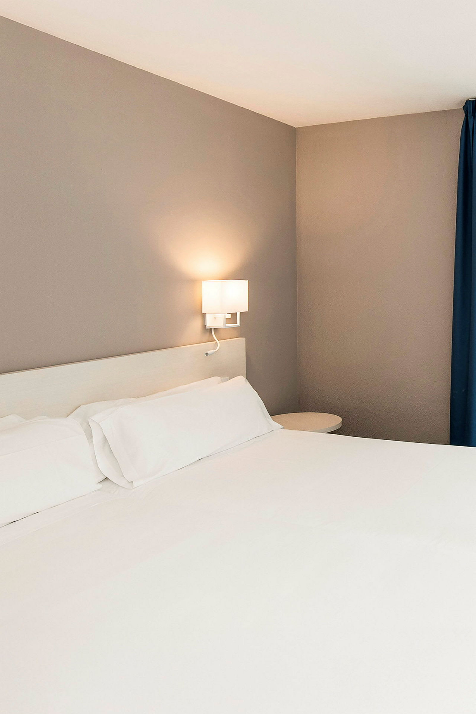 En hotellseng med hvitt sengetøy og vegglampe. (AI-generert tekst)