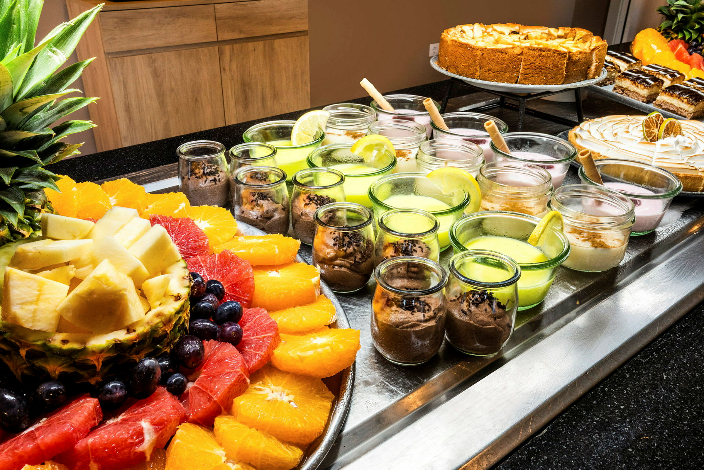 En oppsats med frisk frukt og desserter i små glass. (AI-generert tekst)