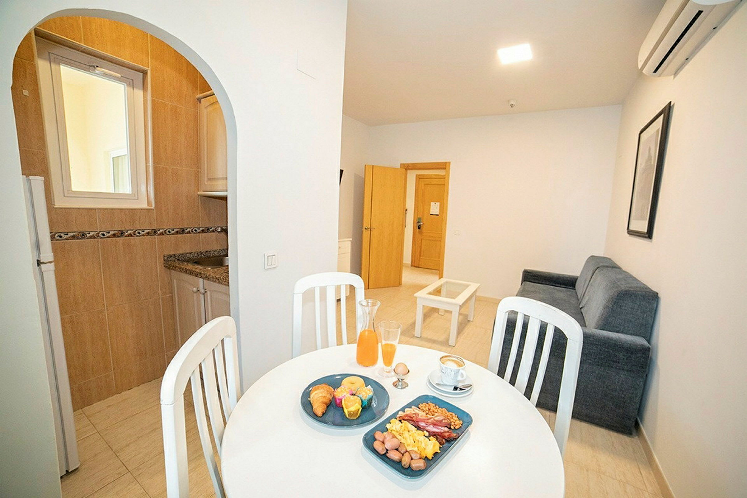 Bilde av en leilighet med kjøkkenkrok og stue, samt et frokostoppdekket bord. (AI-generert tekst)