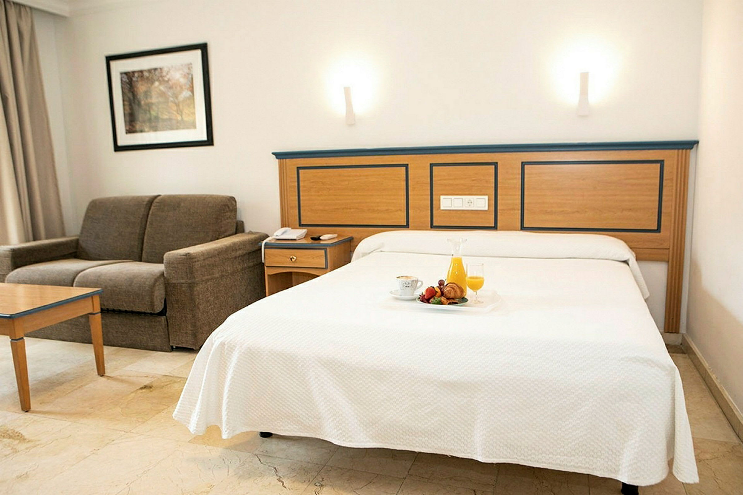 Hotellrom med oppredd seng og sofa. (AI-generert tekst)