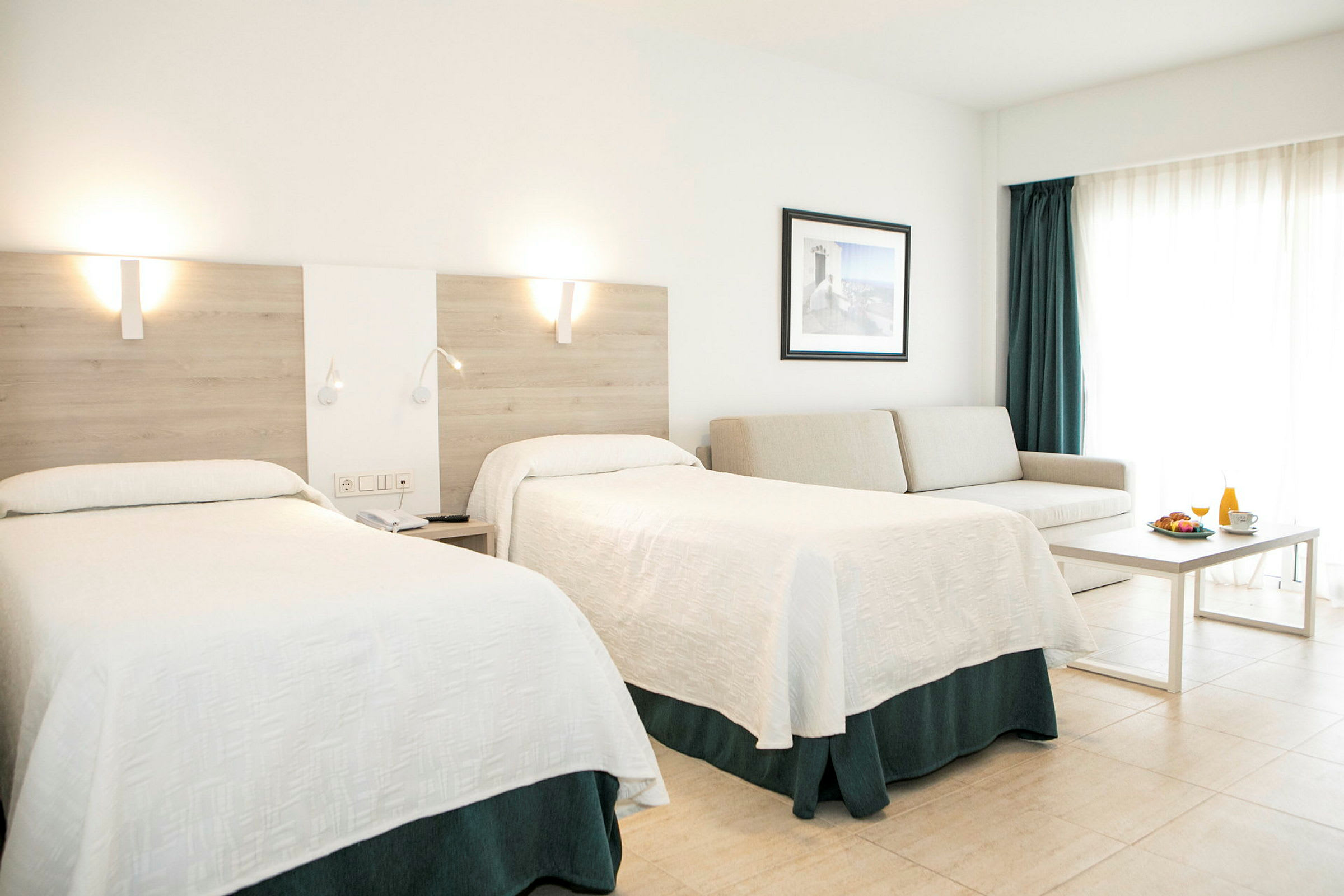 Et hotellrom med to senger, en sofa, et bord og en frokostservering. (AI-generert tekst)