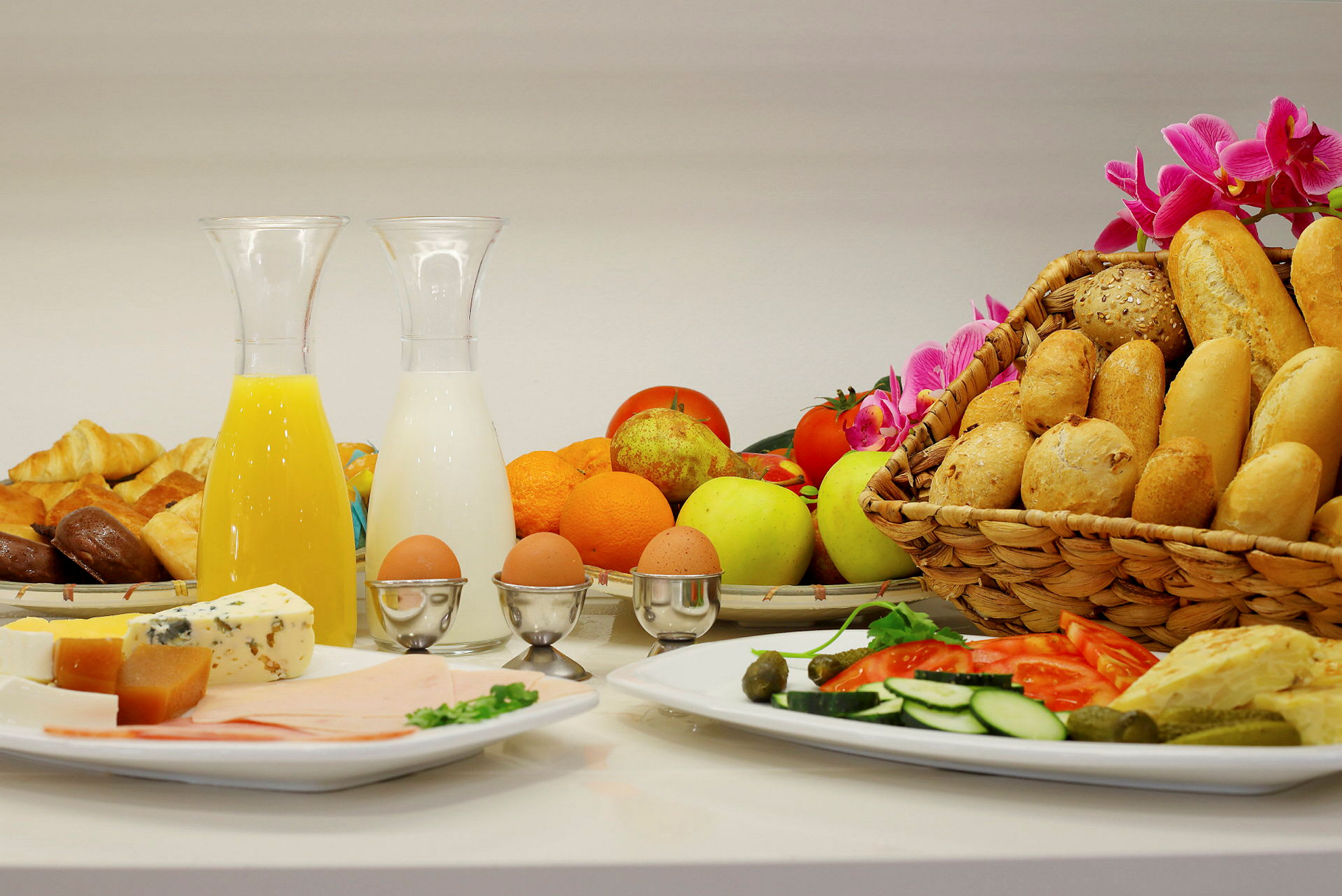 En frokostbuffé med ulike brød, frukt, grønnsaker, ost, pålegg, kokte egg samt drikker som juice og melk. (AI-generert tekst)