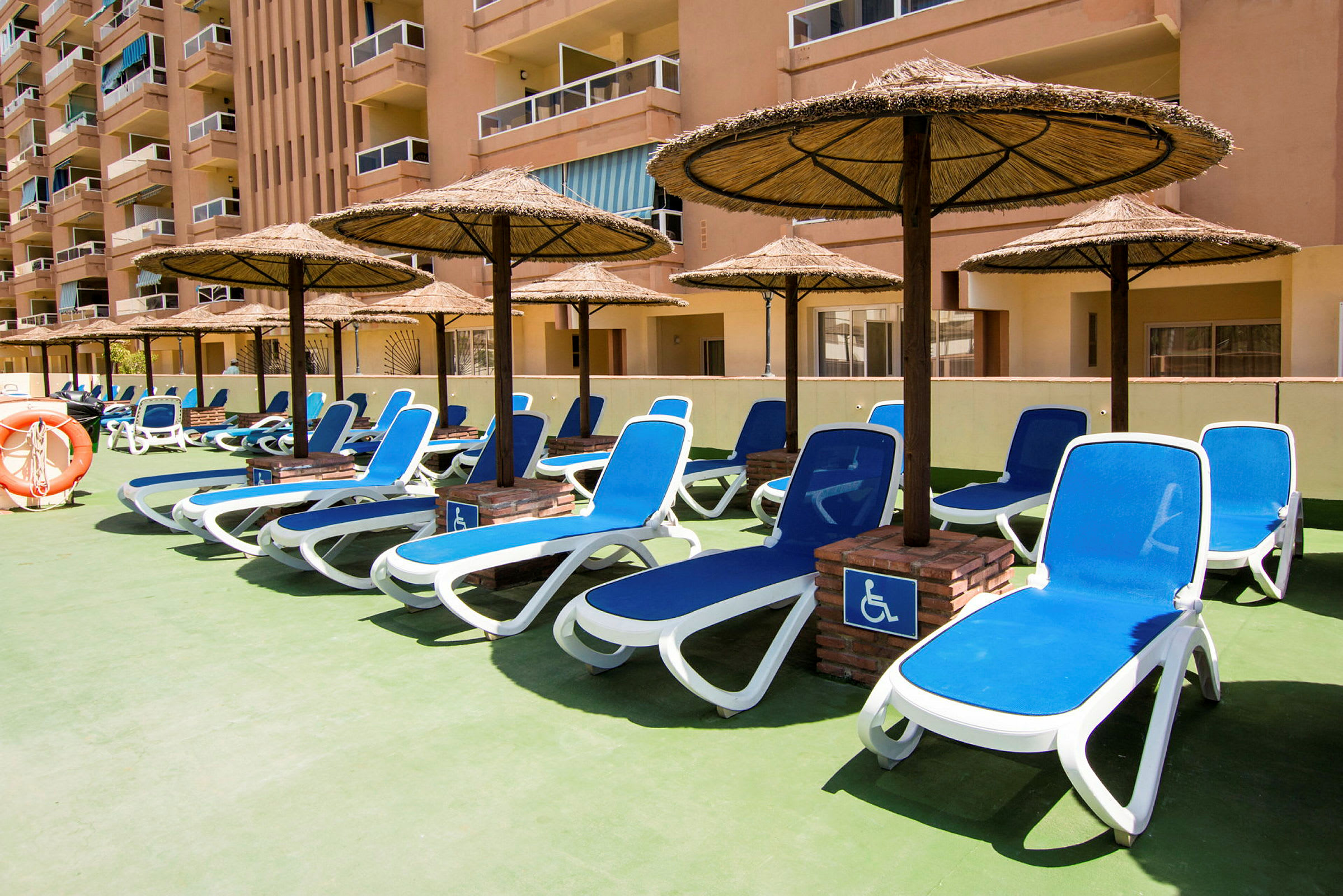 Solstoler med parasoller på en hotellterrasse. (AI-generert tekst)