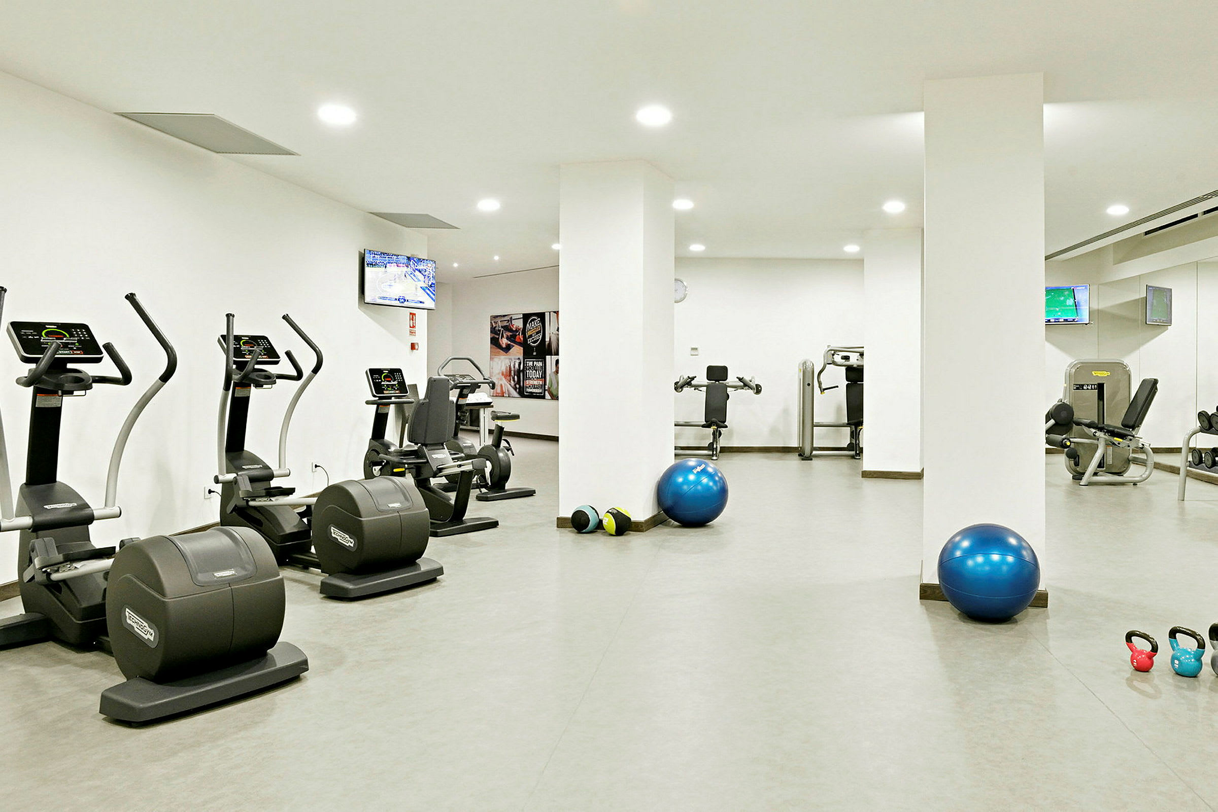 Et treningsrom med treningsmaskiner, treningsballer og kettlebells. (AI-generert tekst)