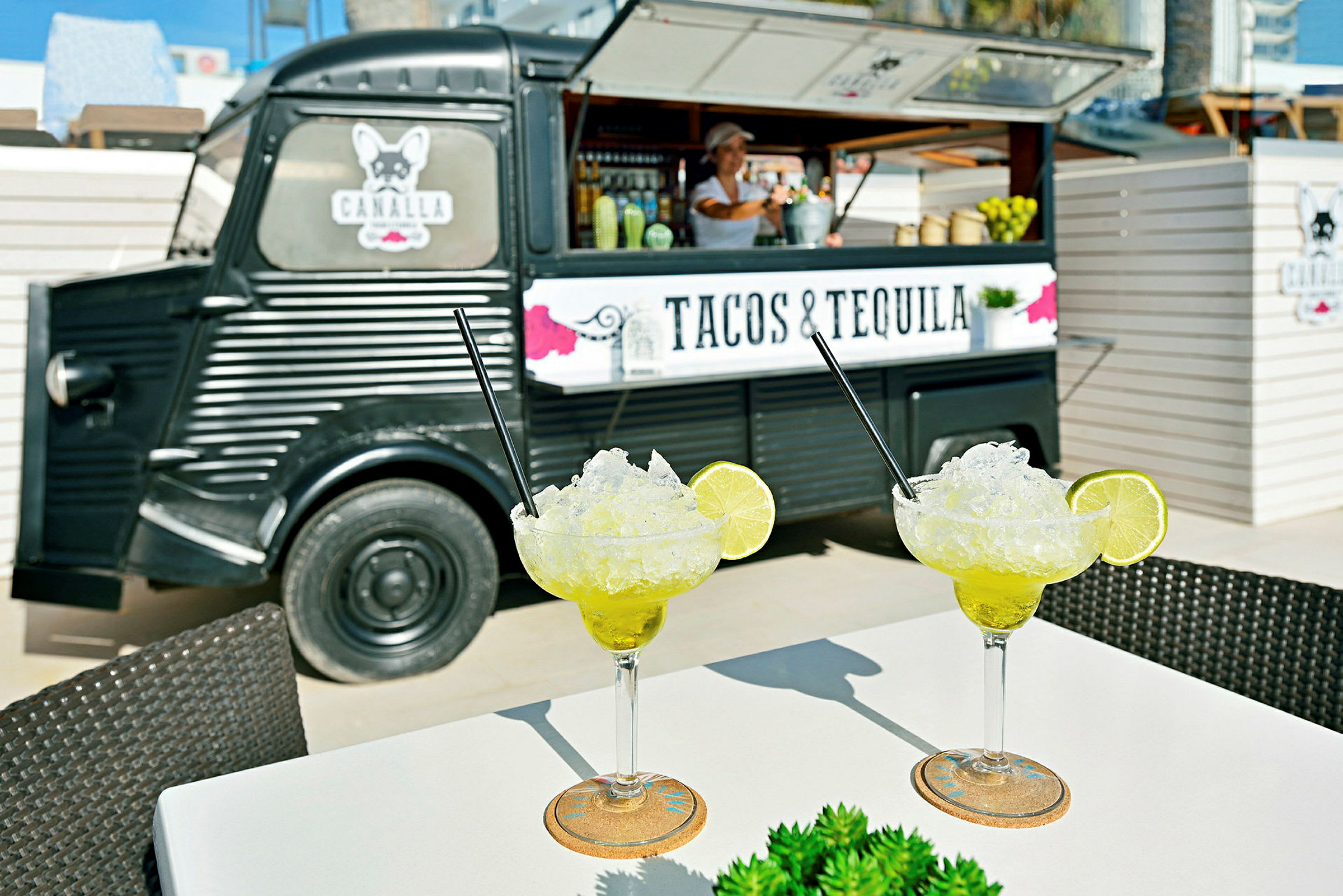 To glass med margaritas står på et bord foran en matbil med teksten "Tacos & Tequila". (AI-generert tekst)