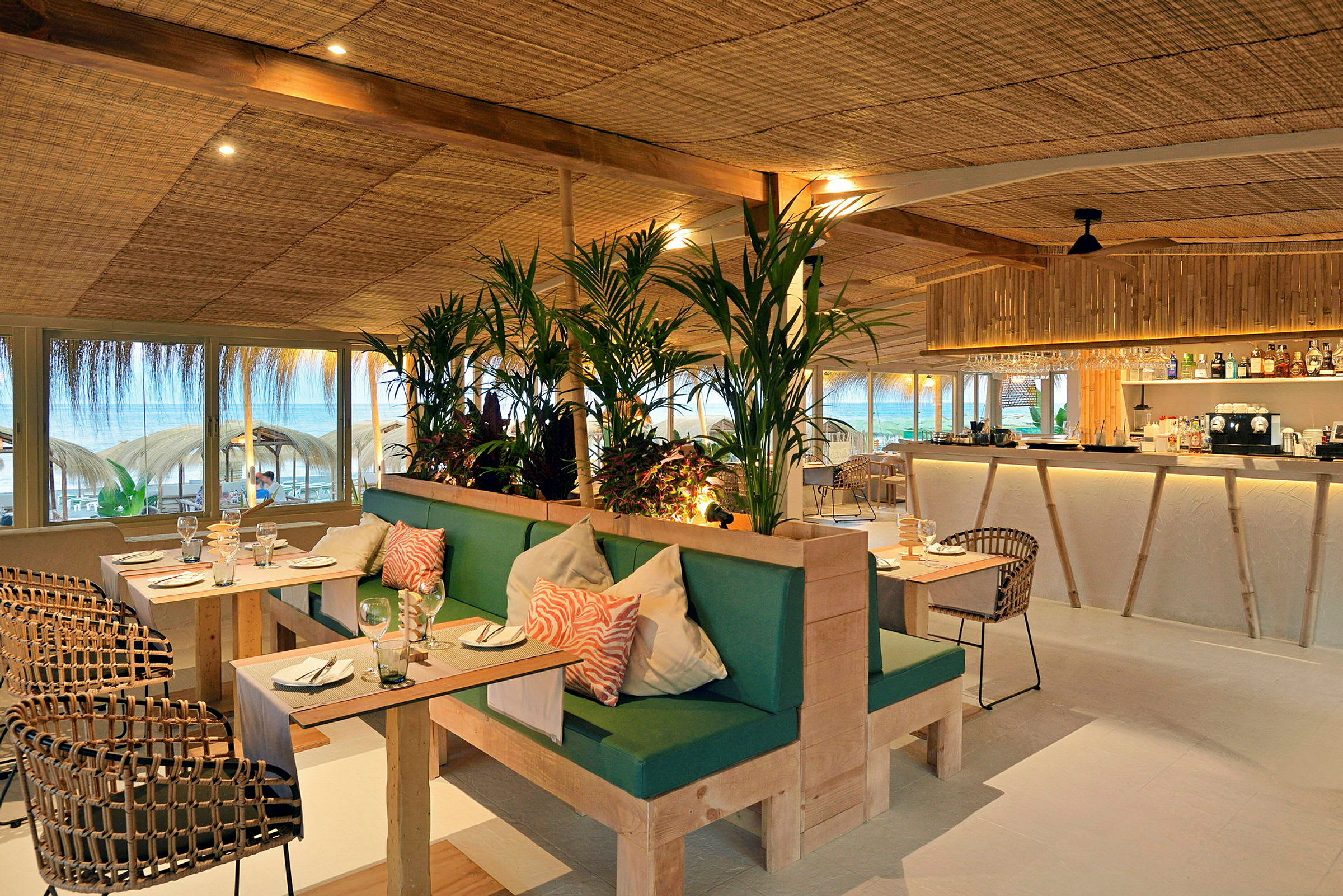 Restaurant med moderne innredning, grønne planter og utsikt mot stranden. (AI-generert tekst)