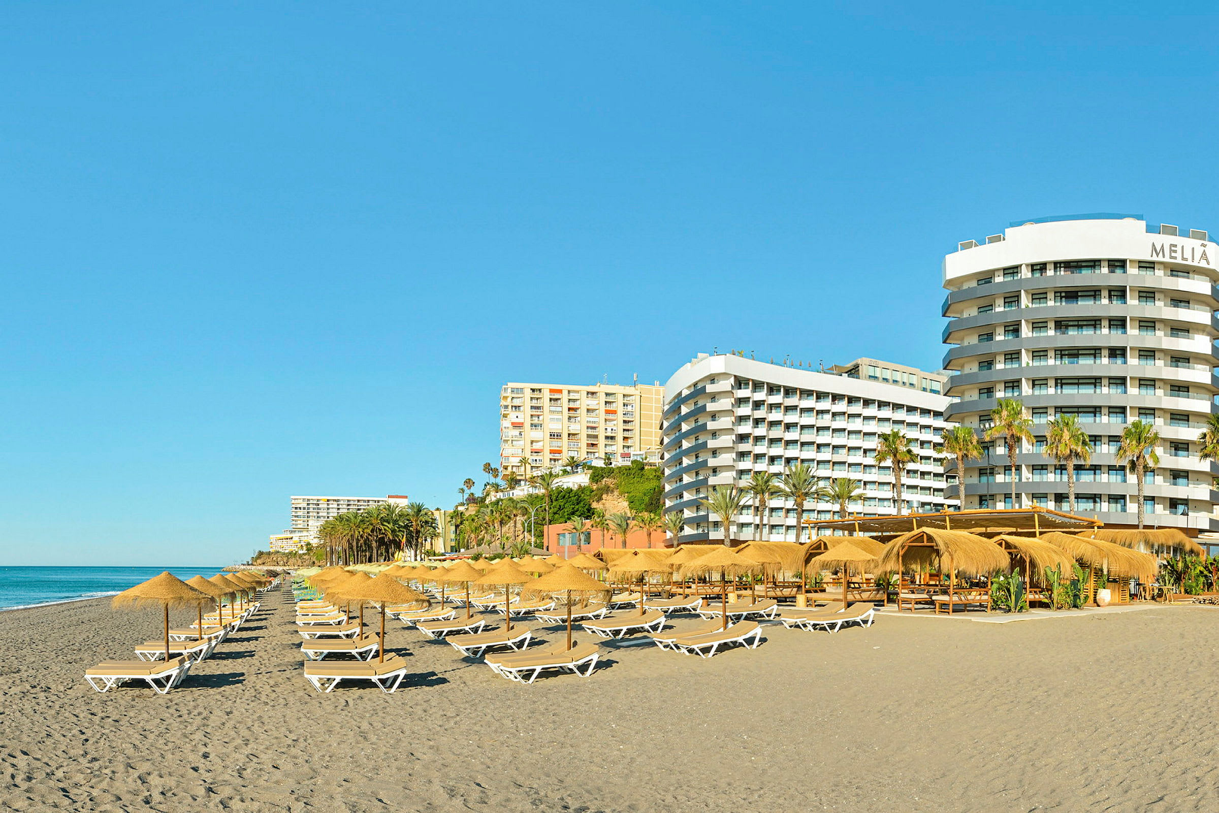 En strand med solsenger og parasoller, omgitt av flere hotellbygninger. (AI-generert tekst)