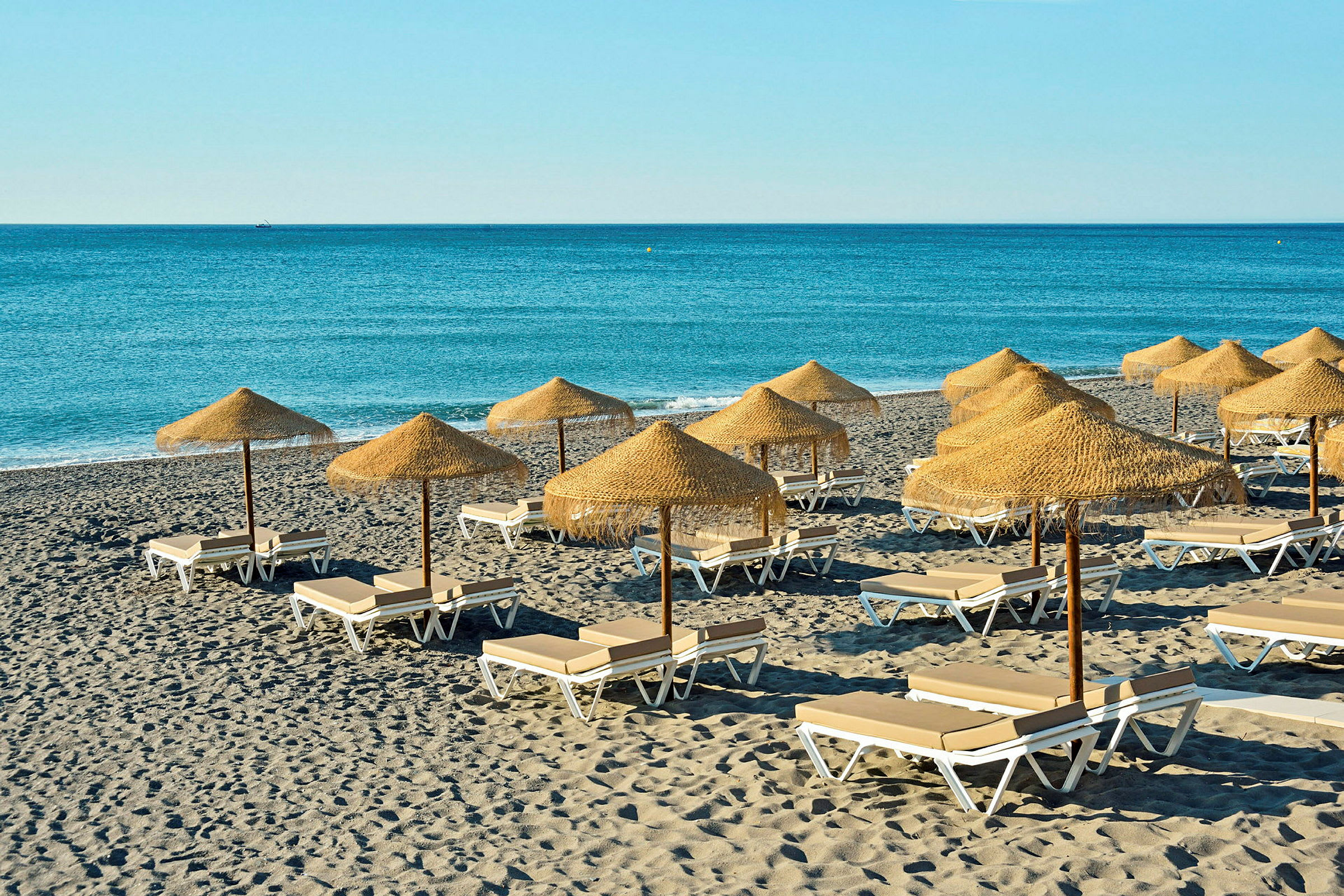 Strand med solsenger og parasoller av tre og strå. (AI-generert tekst)