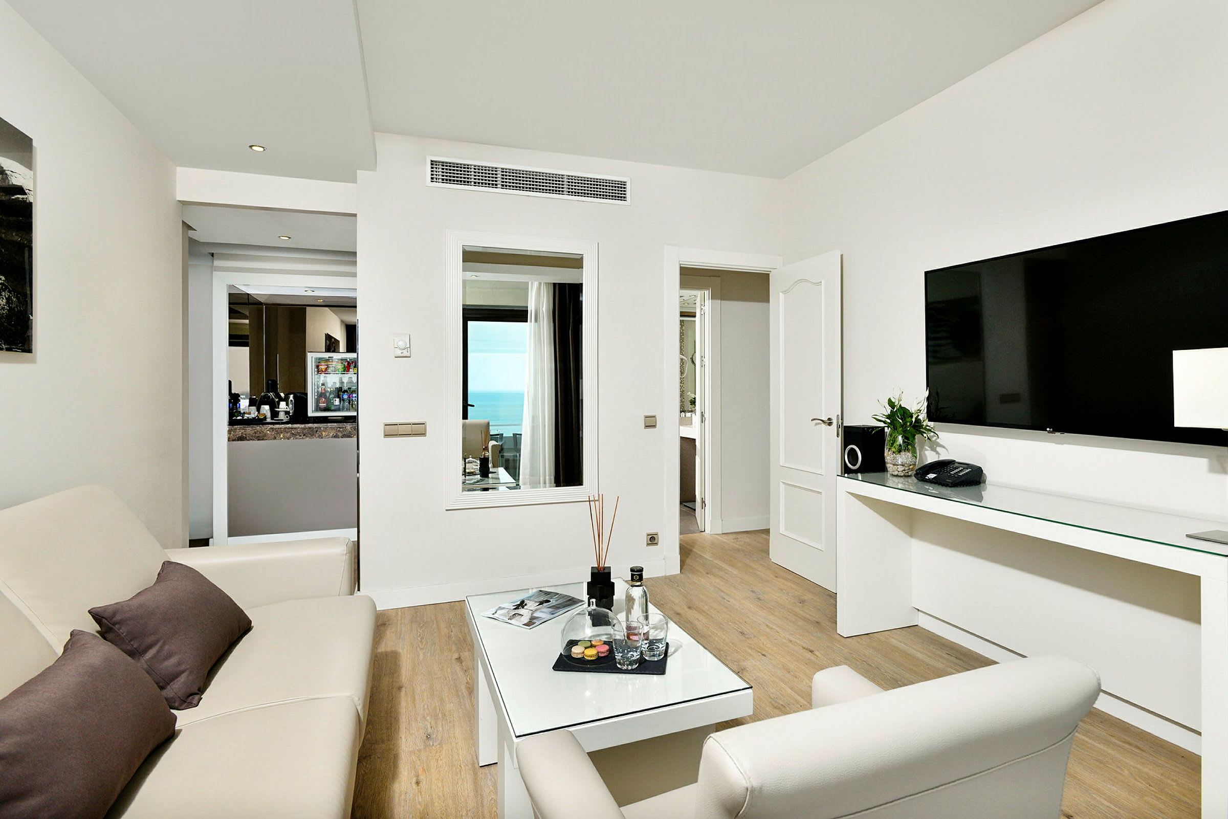 Et hotellrom med stue, sofa, salongbord, stor TV og fin havutsikt. (AI-generert tekst)
