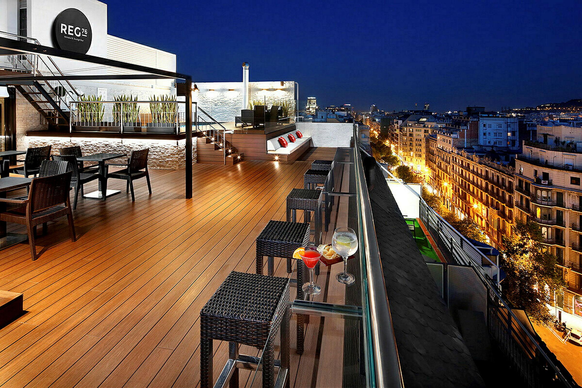 En takterrasse med stoler og bord, kveldopplyst by i bakgrunnen. (AI-generert tekst)