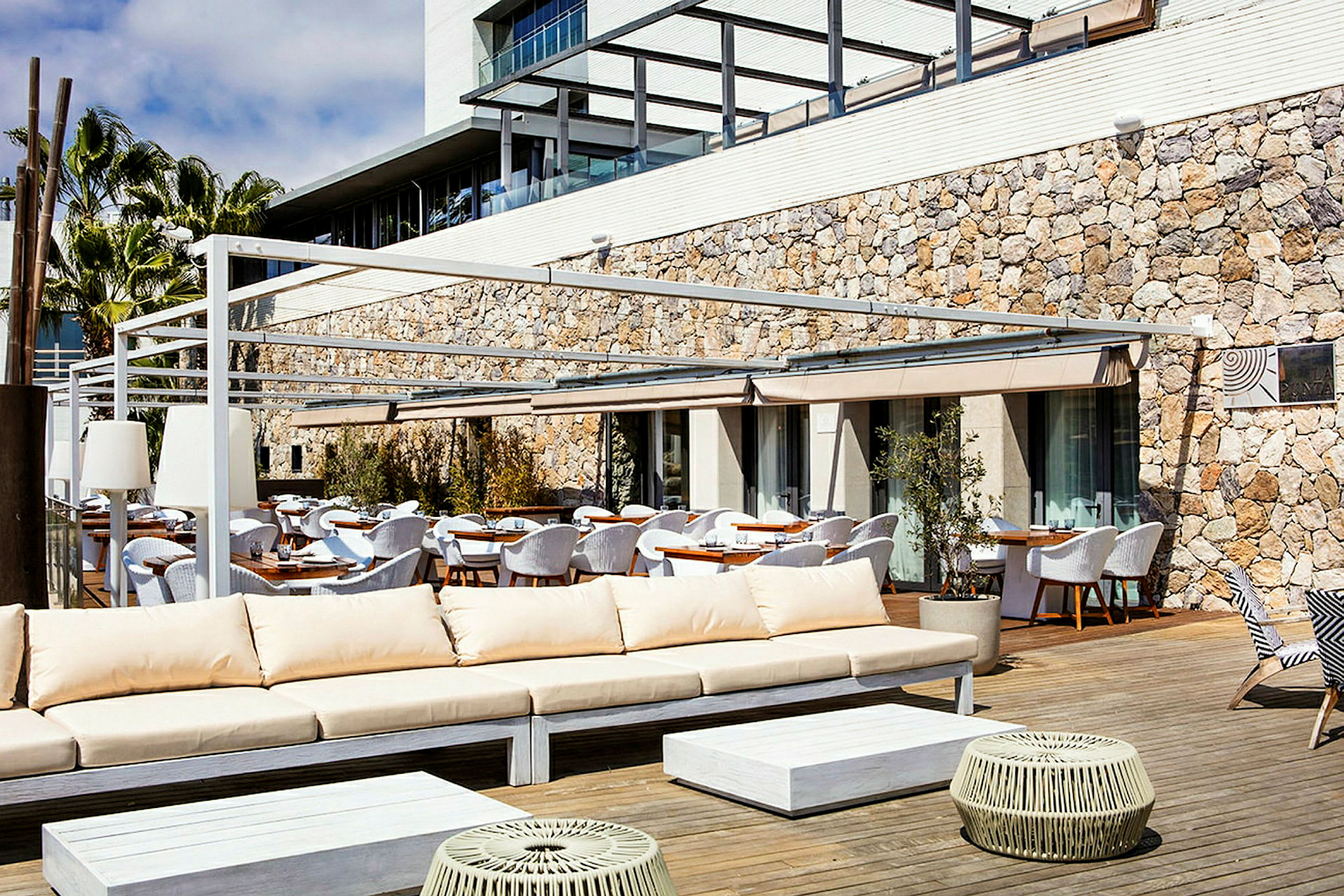 Utendørs loungemøbler og spisebord på en terrasse med steinfasade i bakgrunnen. (AI-generert tekst)