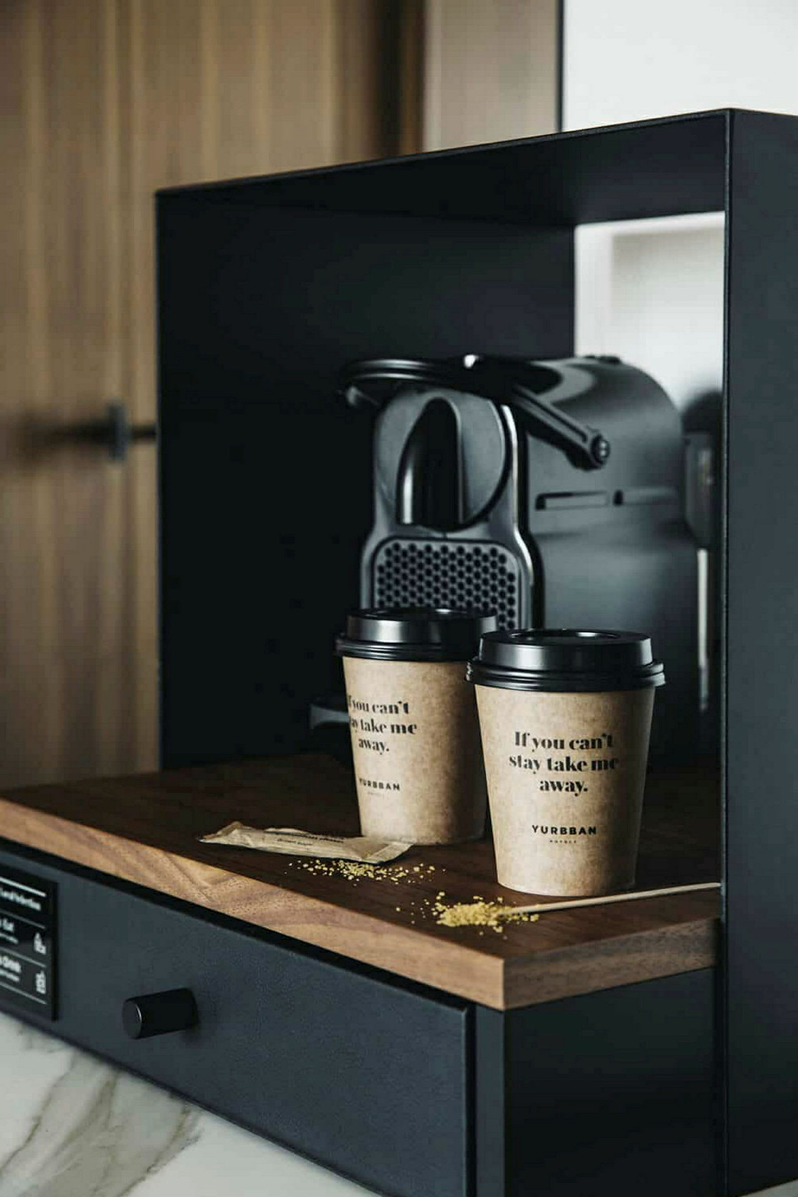 En kaffemaskin står på en mørk trebenk ved siden av to pappkopper med kaffe. (AI-generert tekst)