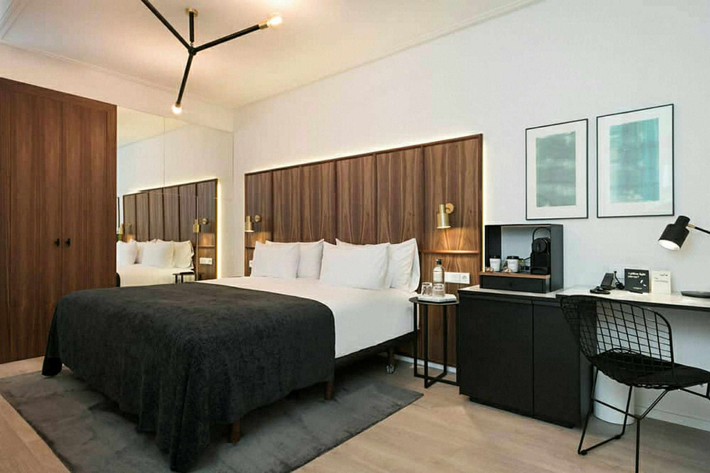 Et moderne hotellrom med en dobbeltseng med mørk sengeteppe, trepanel som hodegavl, en skrivebordkrok med stol og veggkunst, samt et speilskap. (AI-generert tekst)