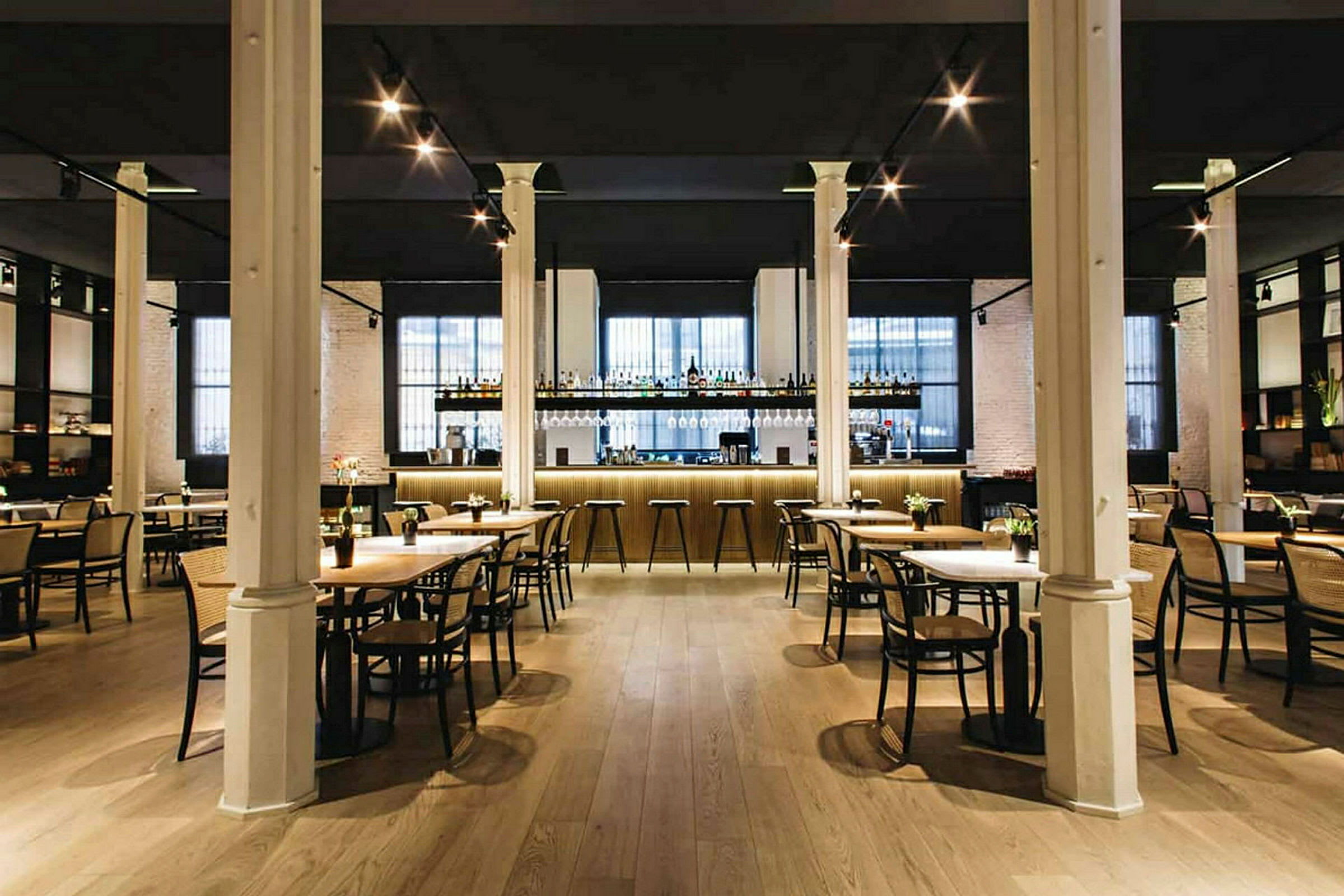 En elegant restaurant med bord og stoler samt en godt opplyst bardisk i bakgrunnen. (AI-generert tekst)