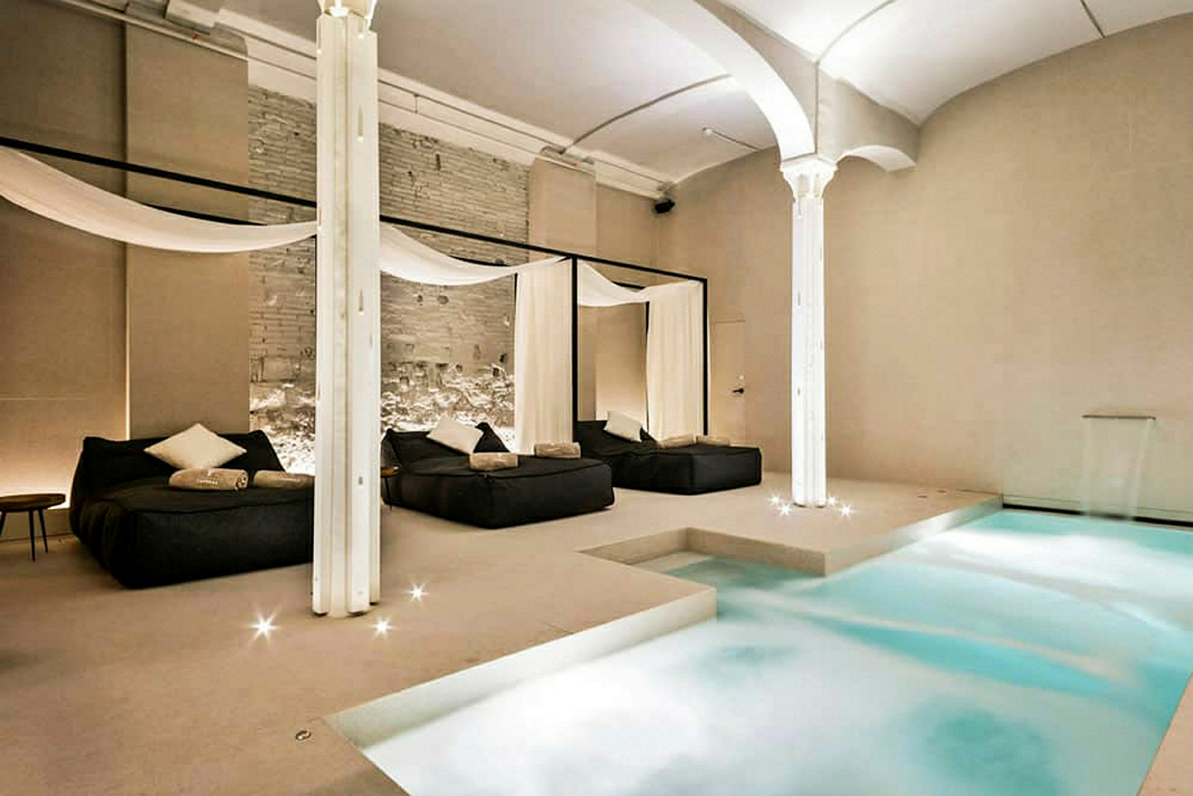 Et elegant innendørs spa med et basseng og avslapningsområder med senger og dekorative draperier. (AI-generert tekst)