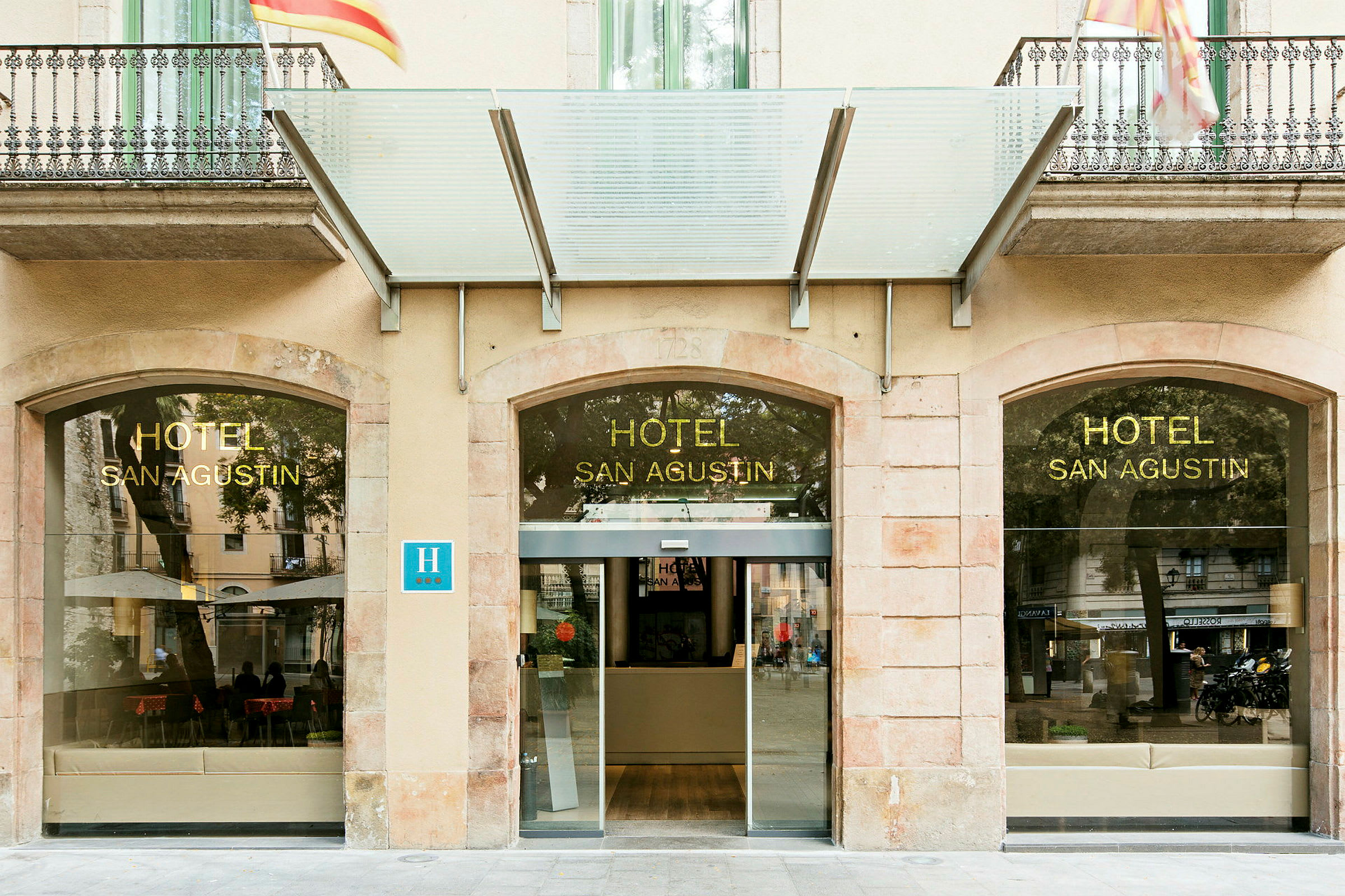 Hotellinngang med glassfasade og skilt med teksten 'HOTEL SAN AGUSTIN'. (AI-generert tekst)