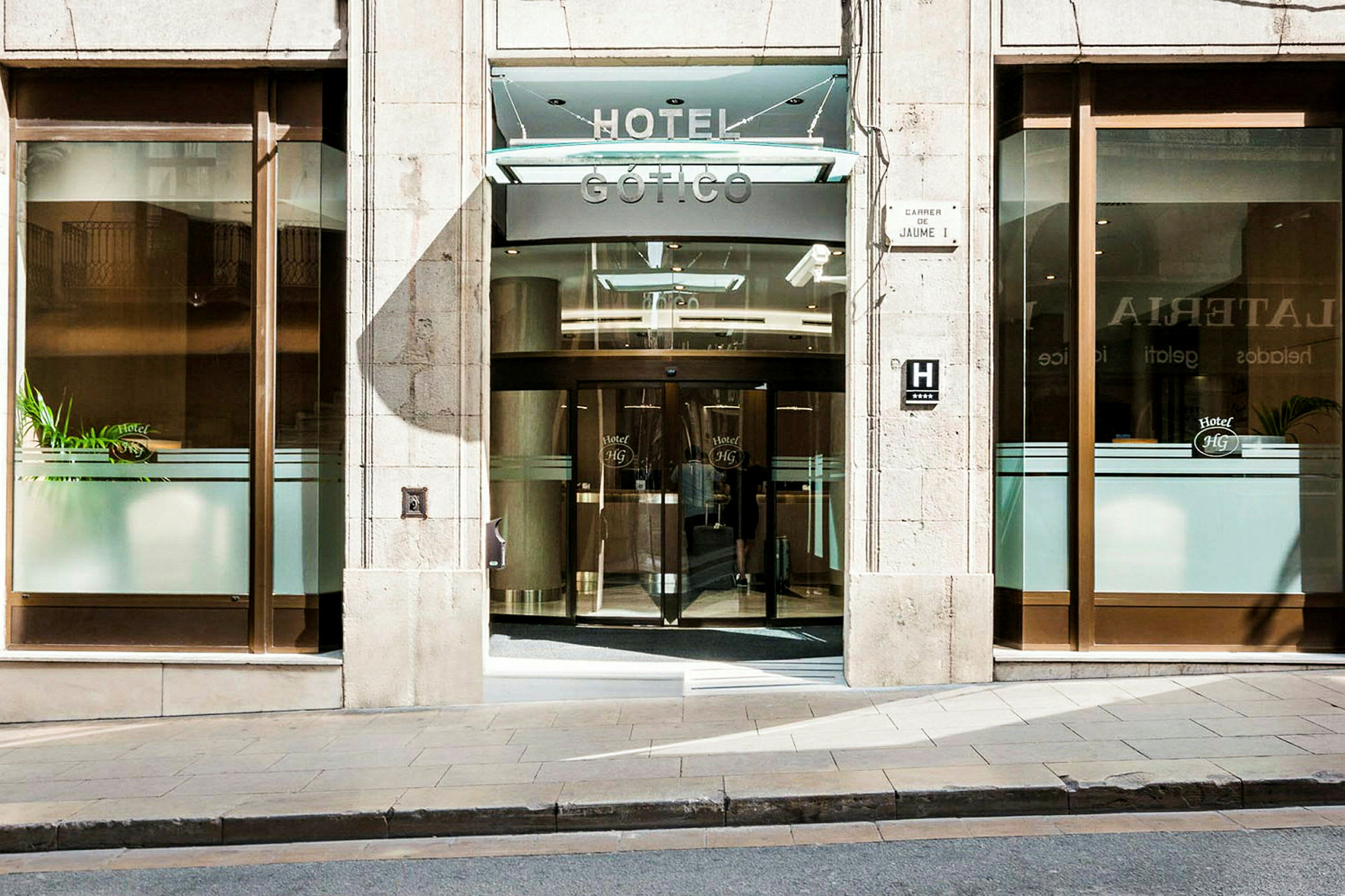 Inngang til et hotell med glassdører og et hotells navn synlig over. (AI-generert tekst)