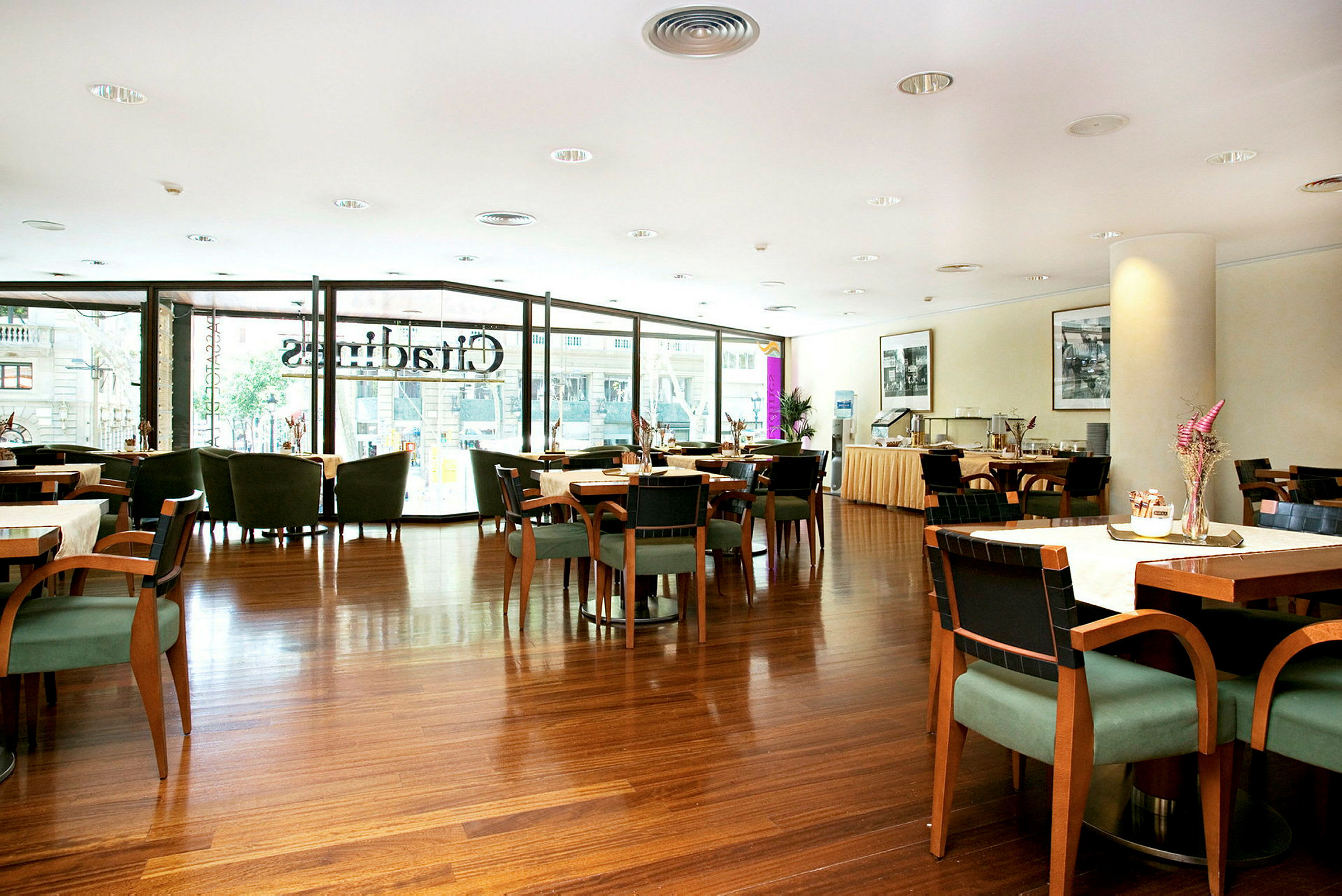 Et innendørsbilde av en elegant restaurant med bord og stoler, hvor store vinduer slipper inn dagslys. (AI-generert tekst)