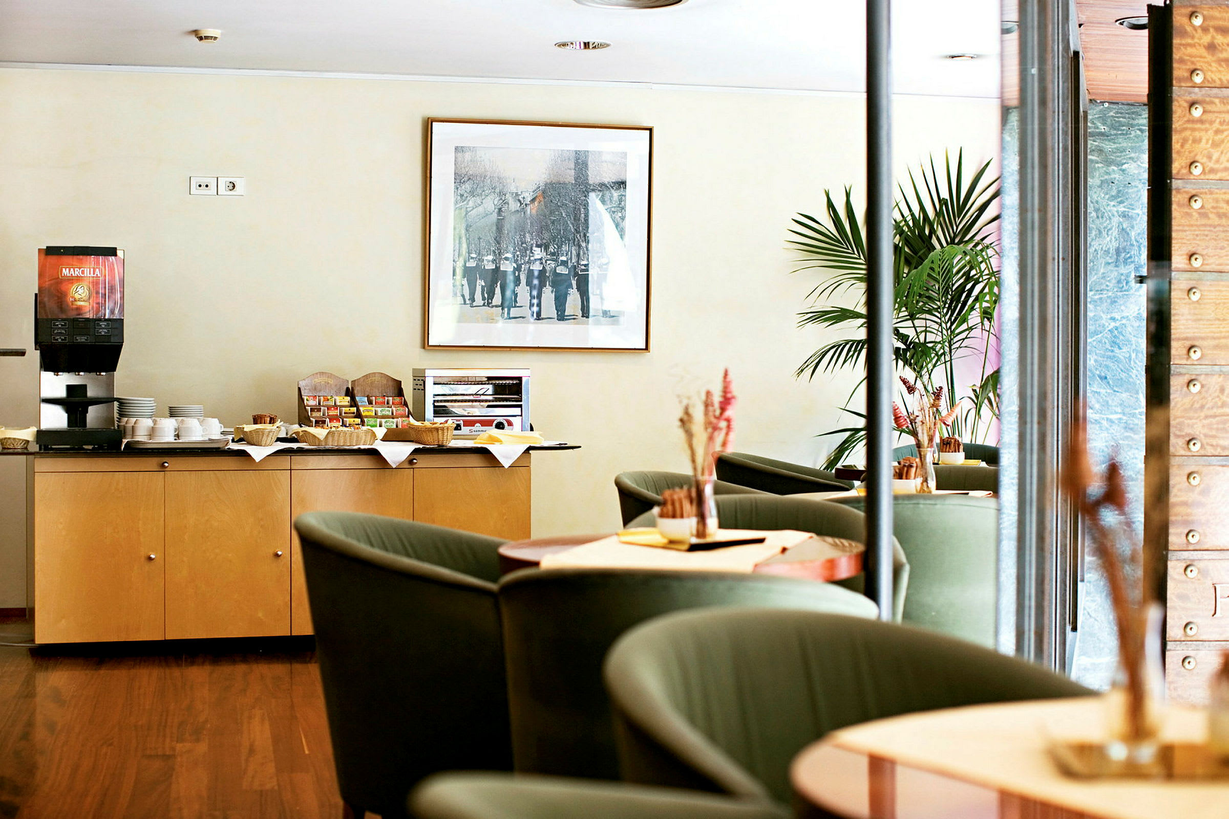 En kaffestasjon og sittegruppe på et hotell eller kafé. En kaffemaskin og snacks er plassert på et skap. (AI-generert tekst)