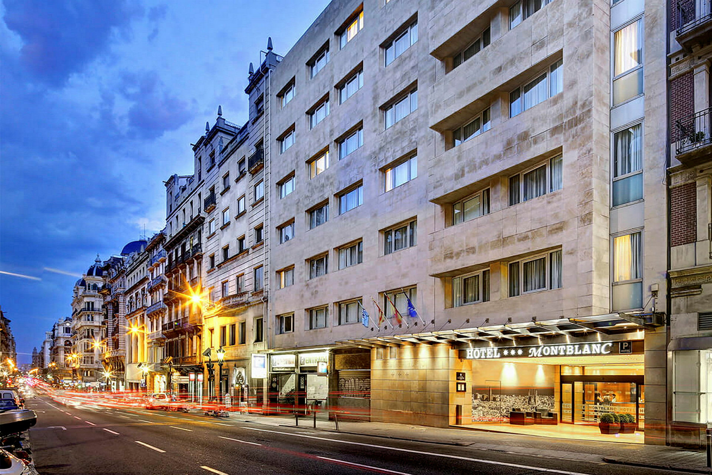 En bygateg med et hotell kalt Montblanc er synlig på høyre side, med flere fasadebygg og kveldsbelysning. (AI-generert tekst)