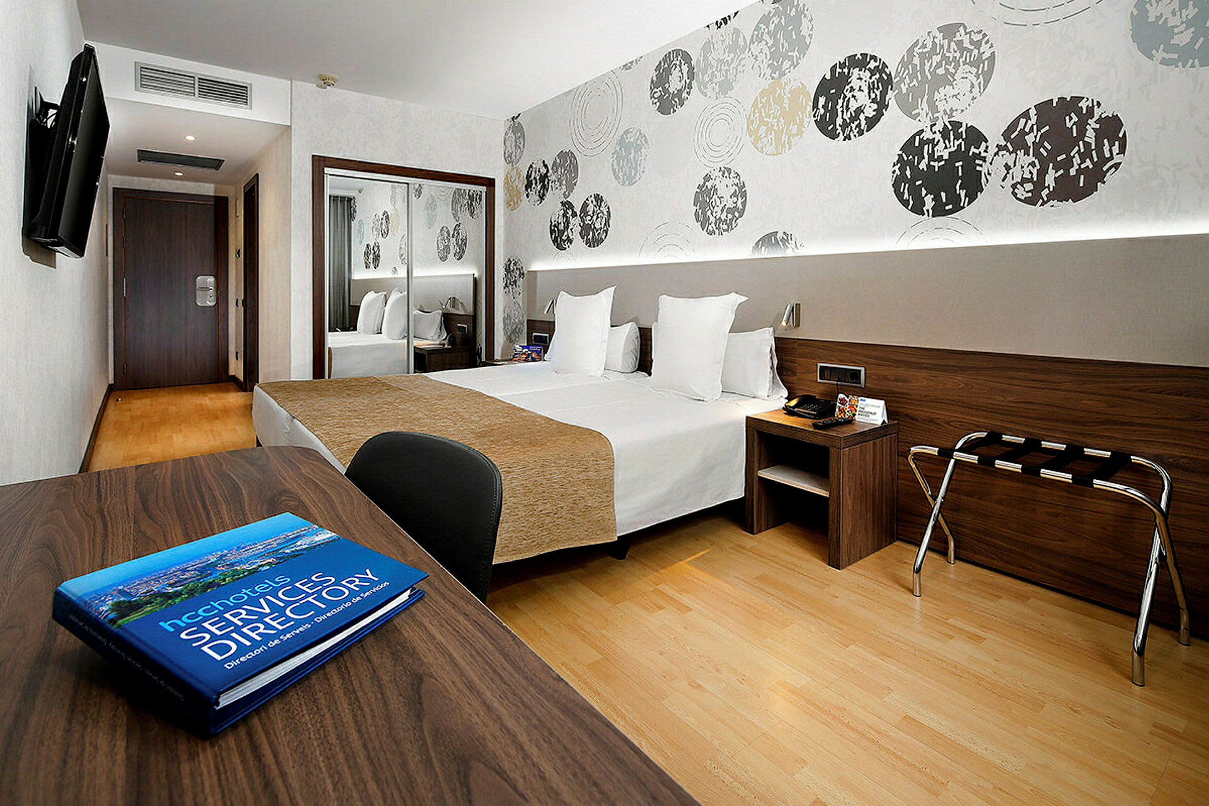 Et moderne hotellrom med to senger, et skrivebord og en abstrakt dekorert vegg. (AI-generert tekst)