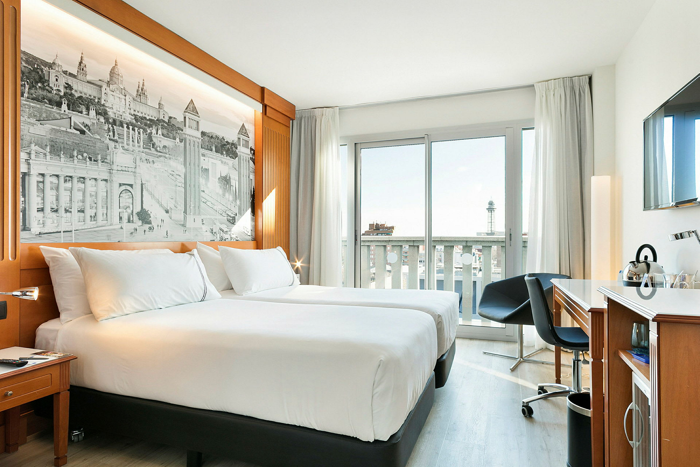 Hotellrom med to enkeltsenger, et arbeidsområde og et vindu med balkongutsikt. (AI-generert tekst)