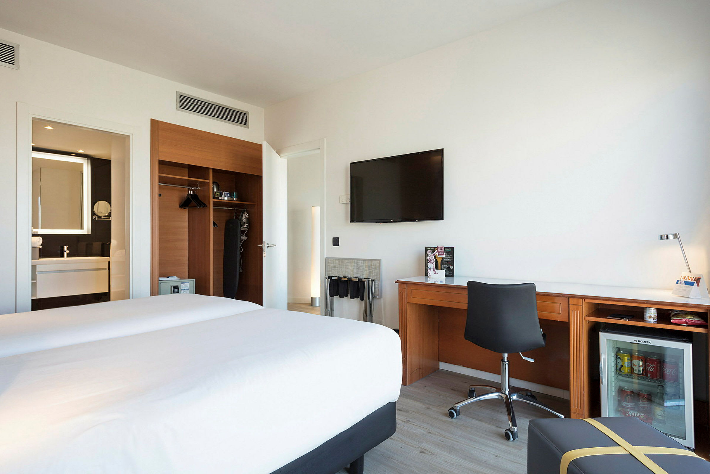 Hotellrom med to senger, en arbeidsplass og et skap samt bad i bakgrunnen. (AI-generert tekst)