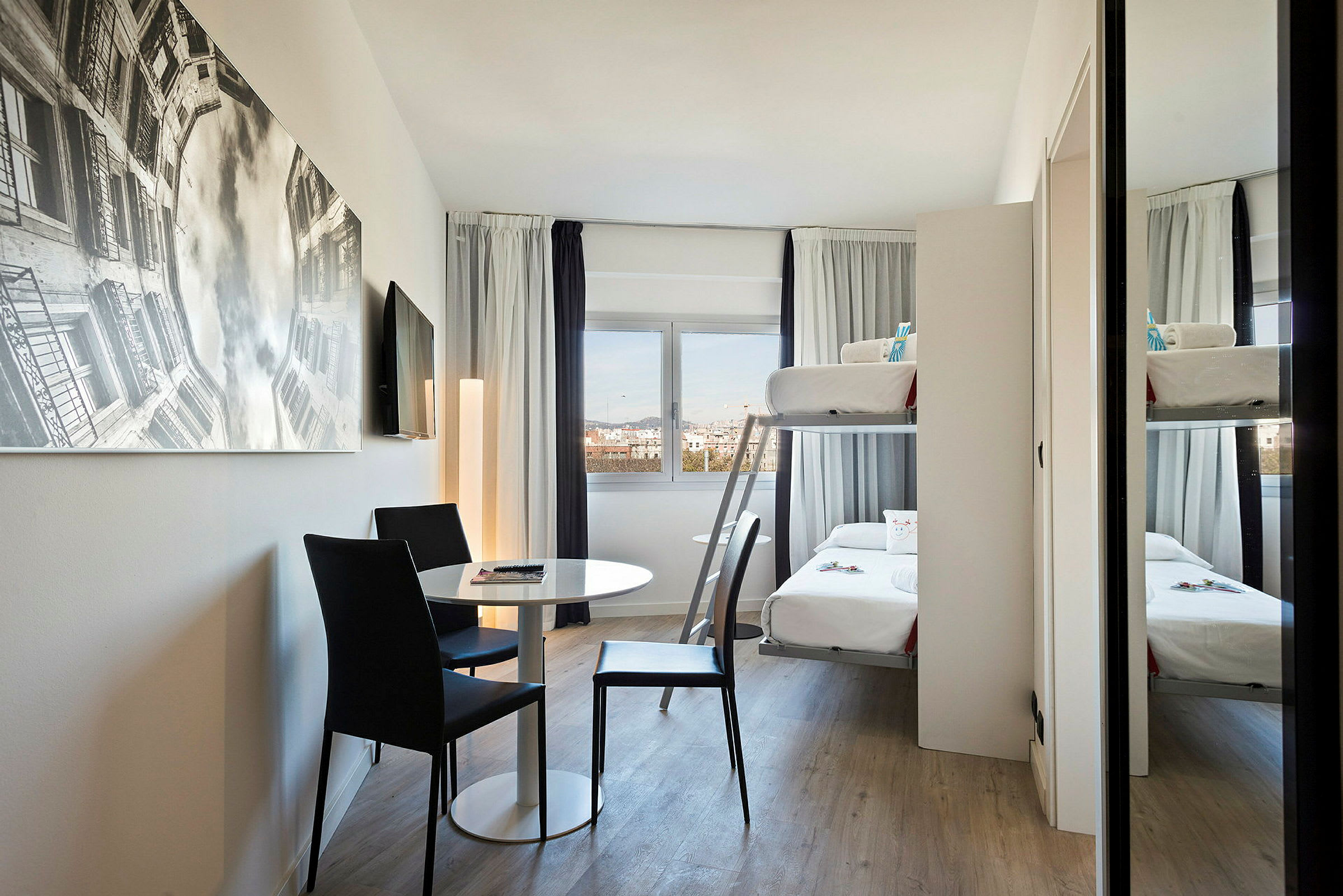 Et moderne hotellrom med køyeseng, bord og to stoler samt et stort veggbilde. (AI-generert tekst)